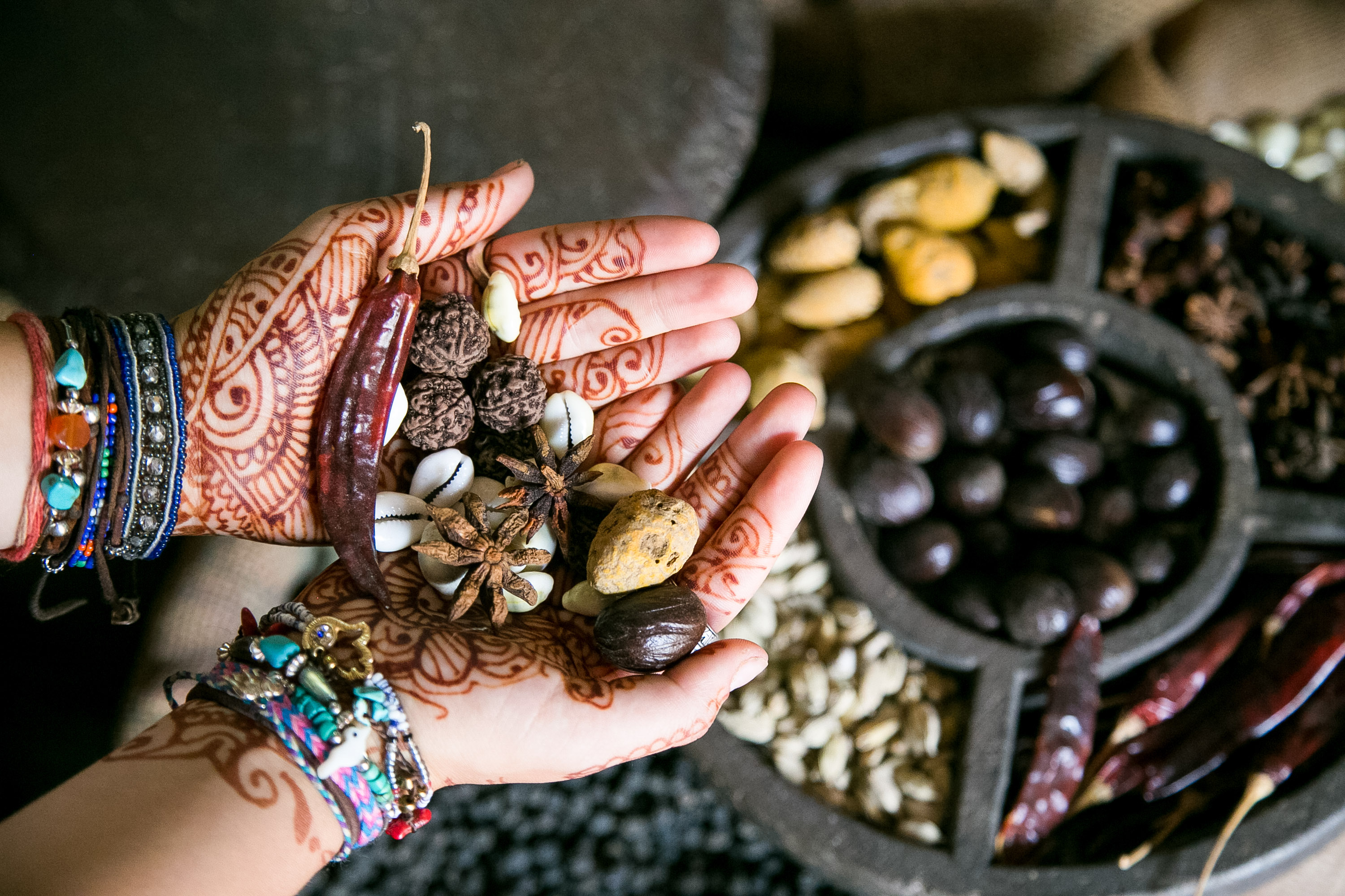 Henna-decorated hands hold whole spices beside a spice tray