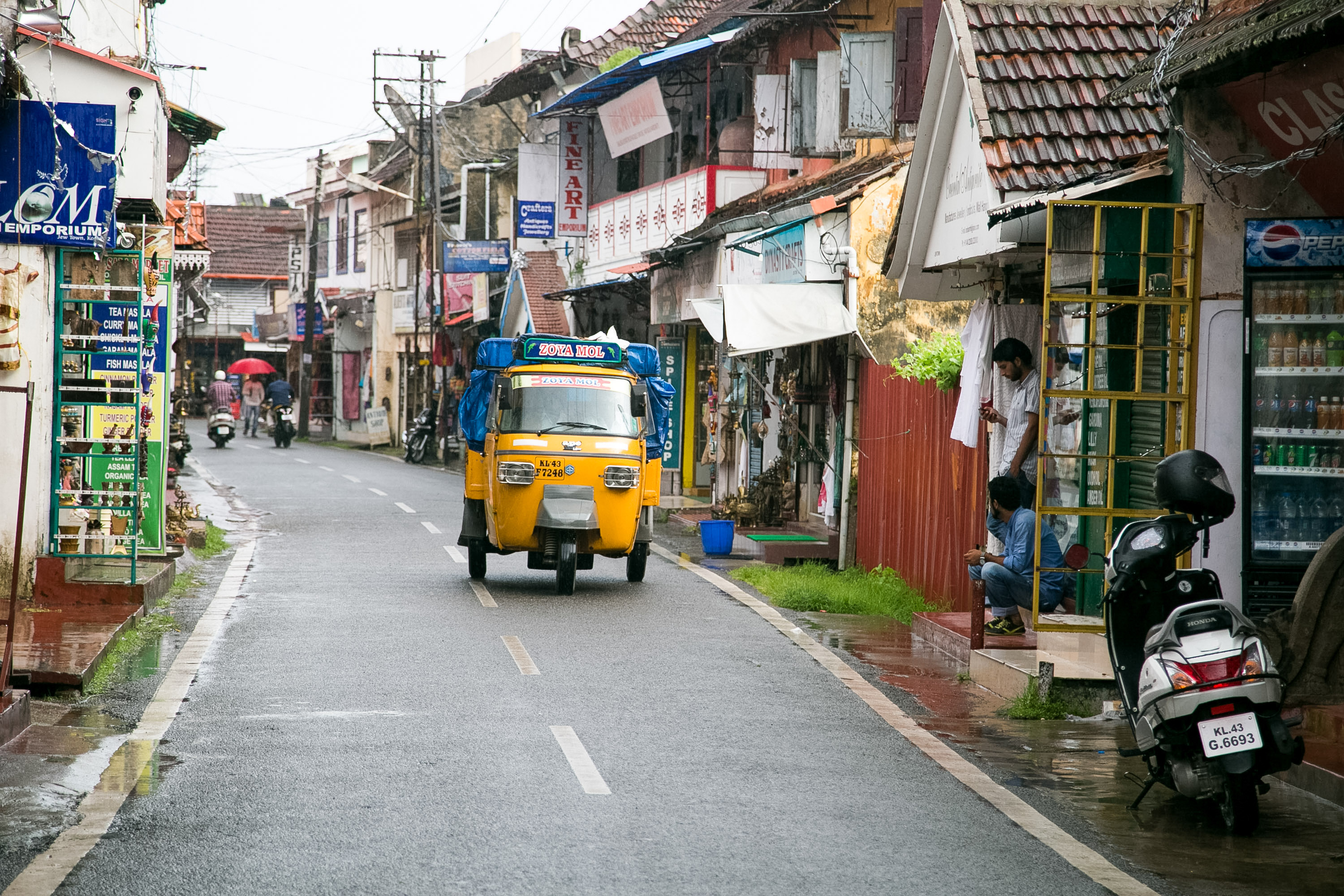 An auto rickshaw drives down a rain-slicked street lined with shops