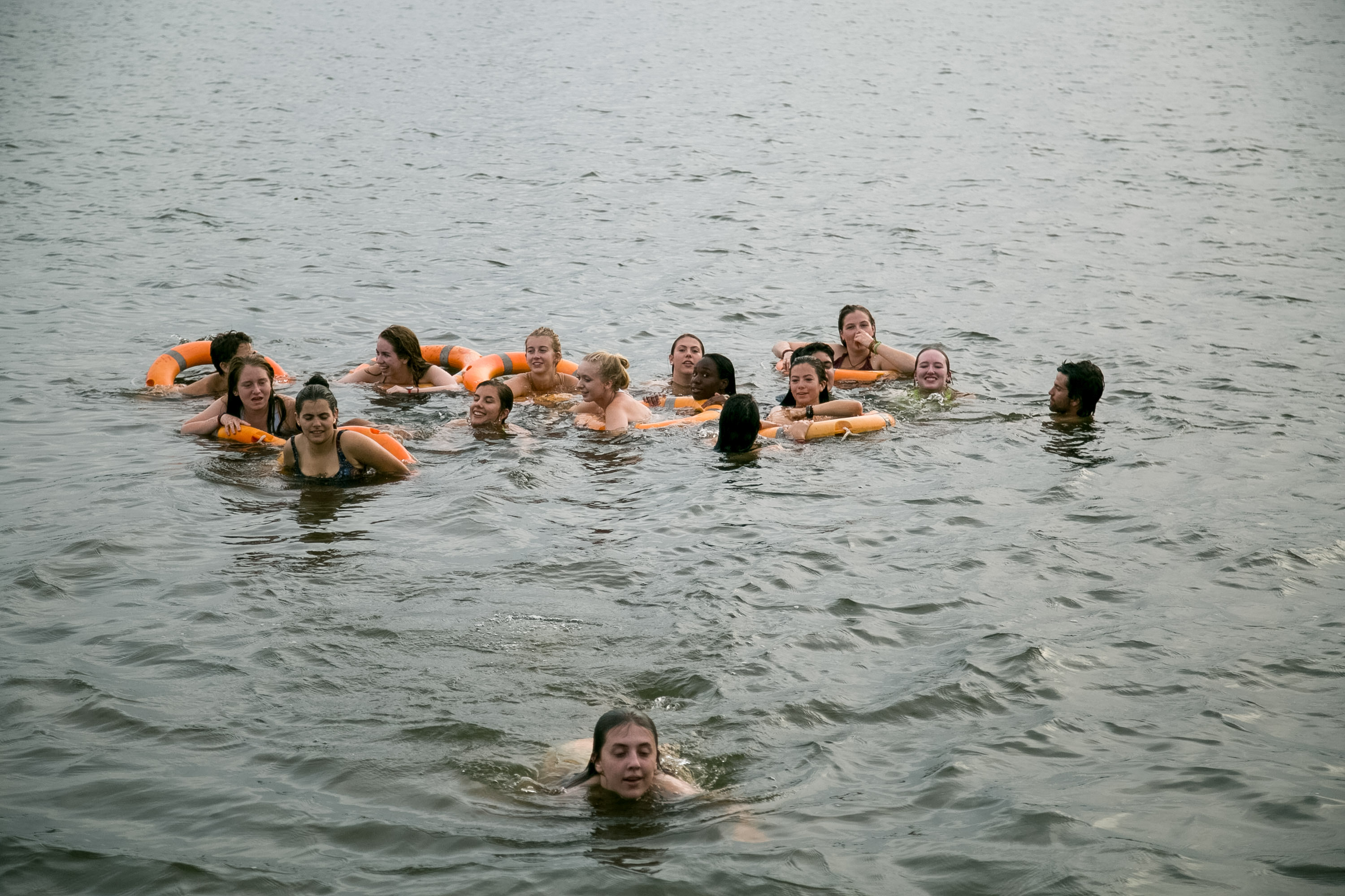 Students swim together in a lake using orange flotation rings