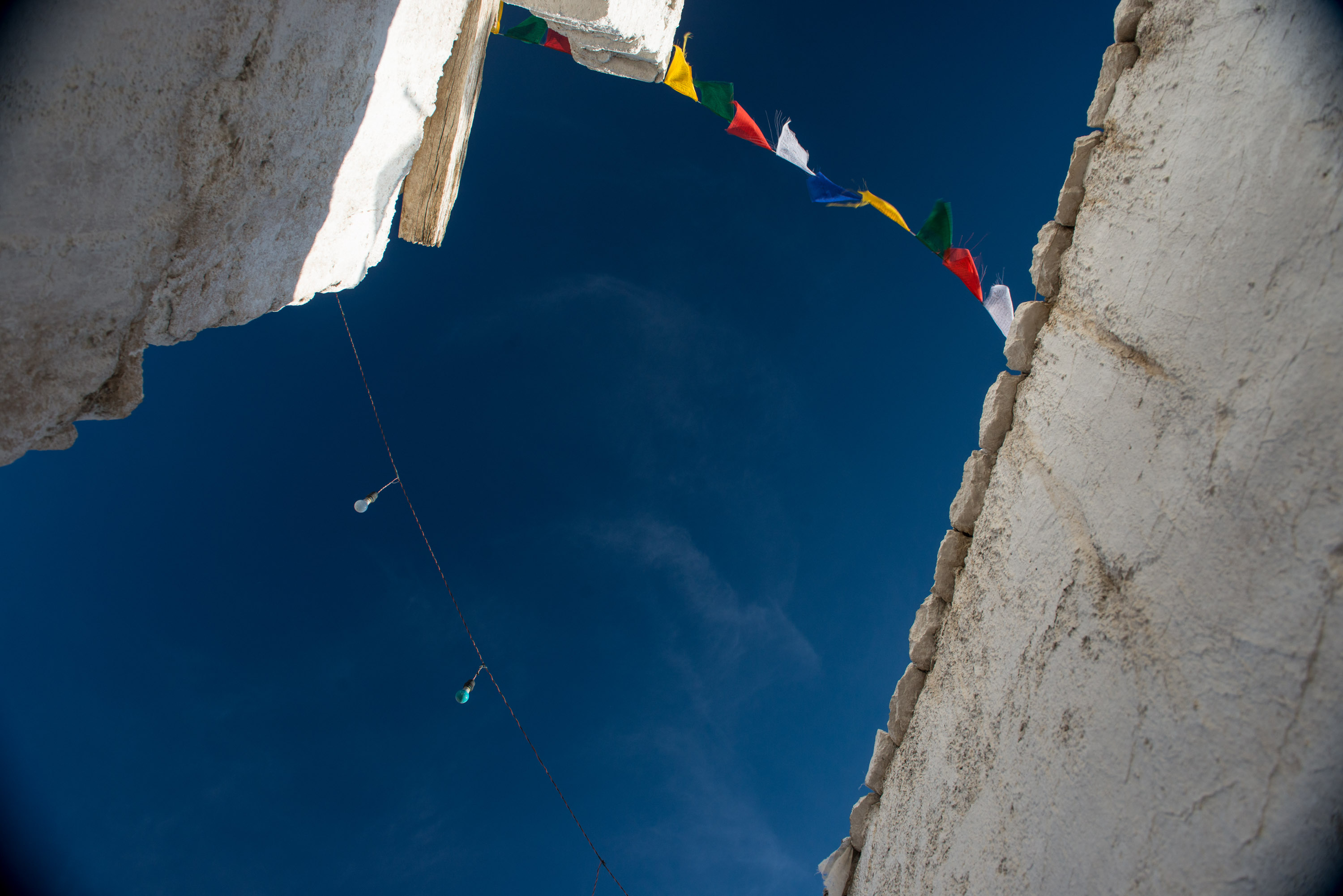 Prayer flags strung between weathered stone walls against a blue sky