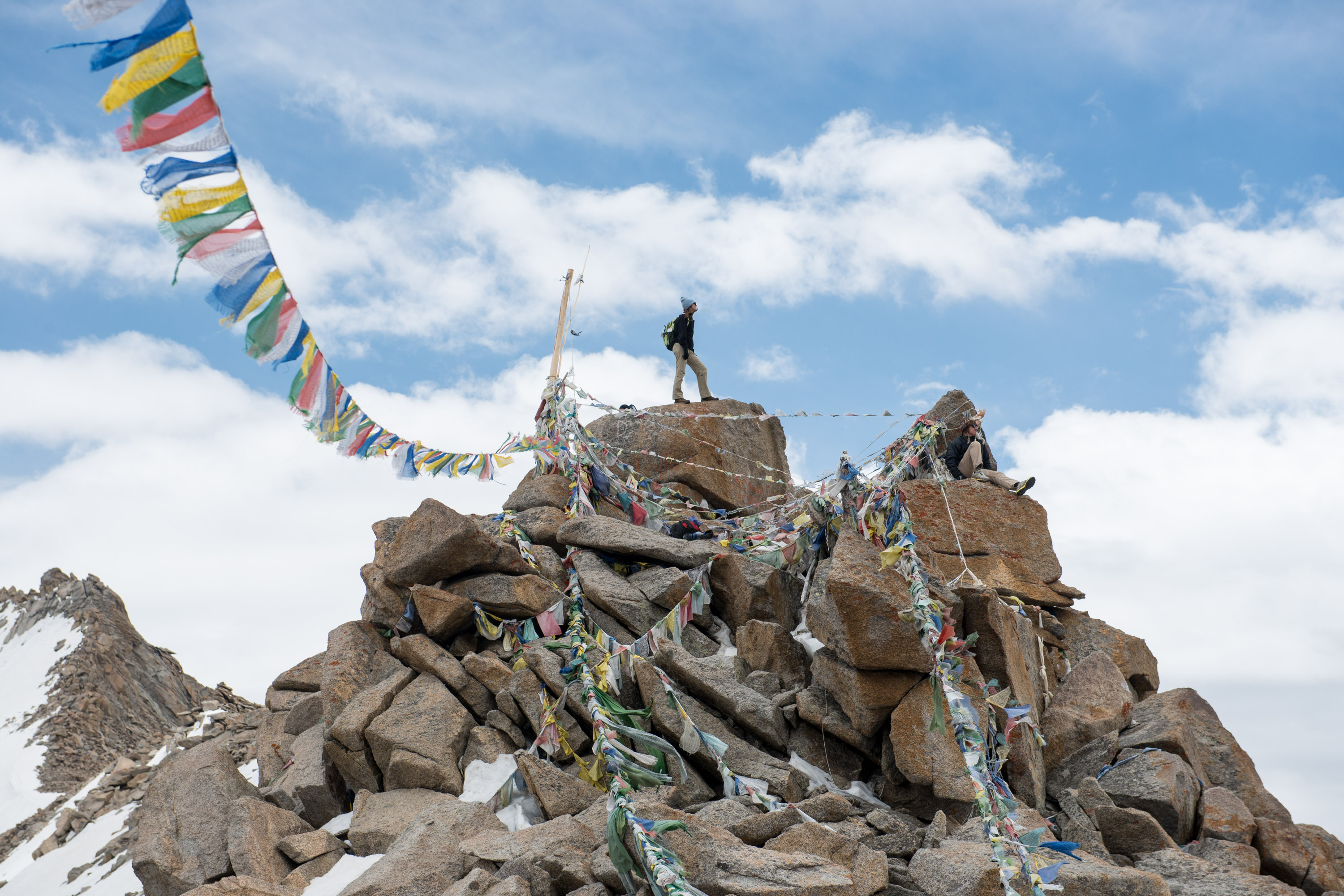 A student stands atop a rocky peak strung with colorful prayer flags