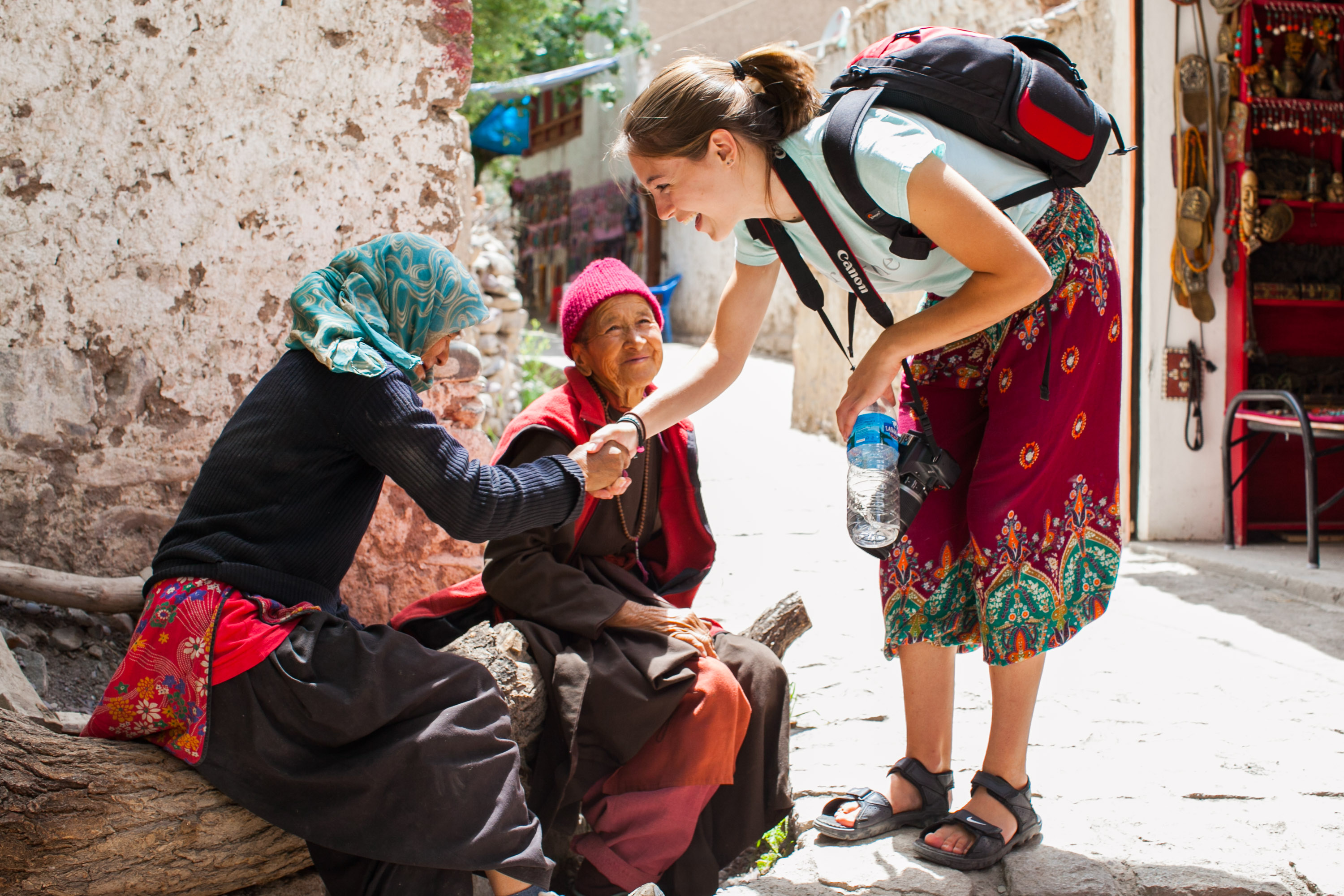 A student greets local women with a handshake on a shaded street in Nepal