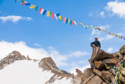 A teen traveler sits on an outcrop in the Nepalese mountains surrounded by prayer flags during a teen tour in Asia.