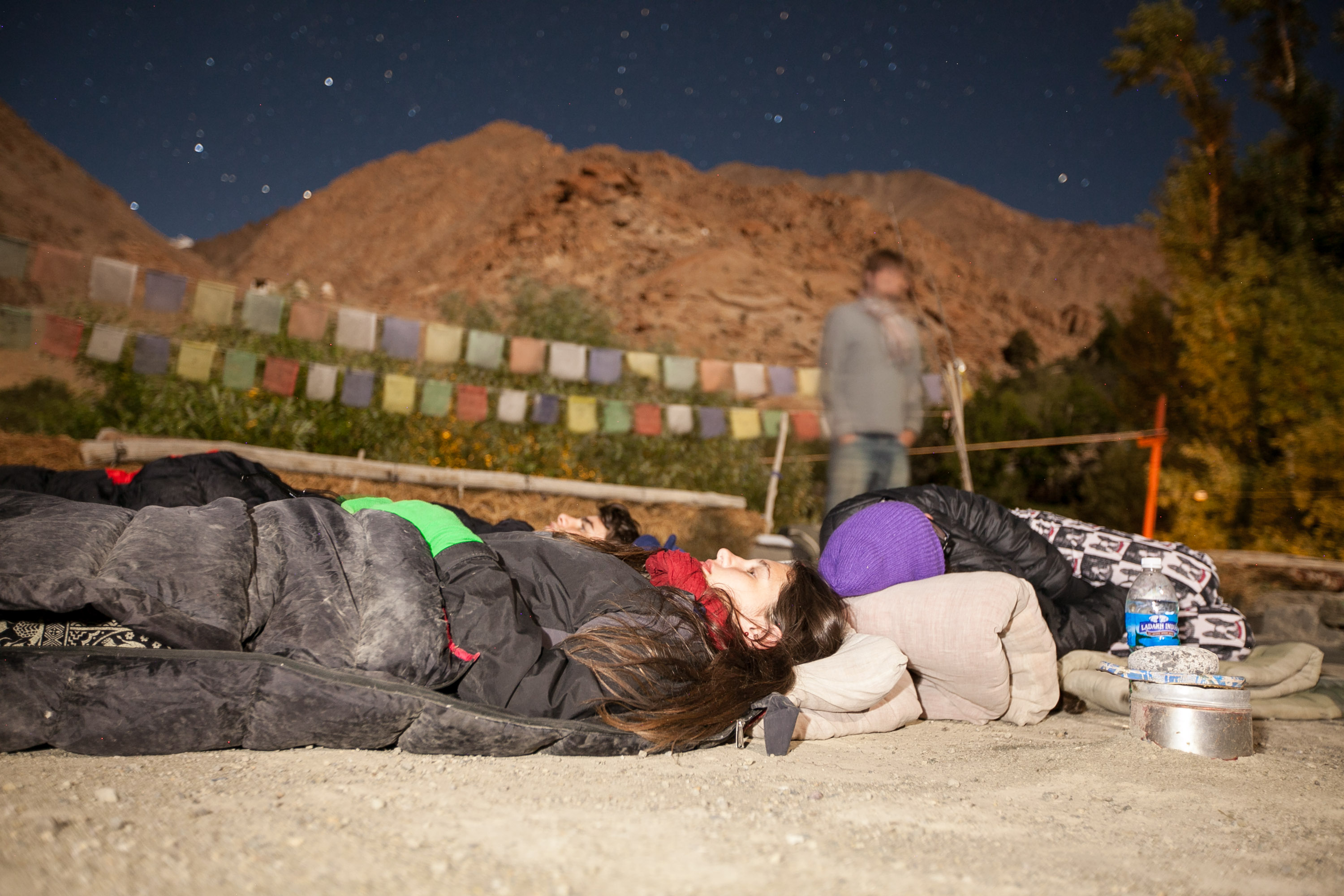Students lie in sleeping bags stargazing beneath mountains strung with prayer flags at night