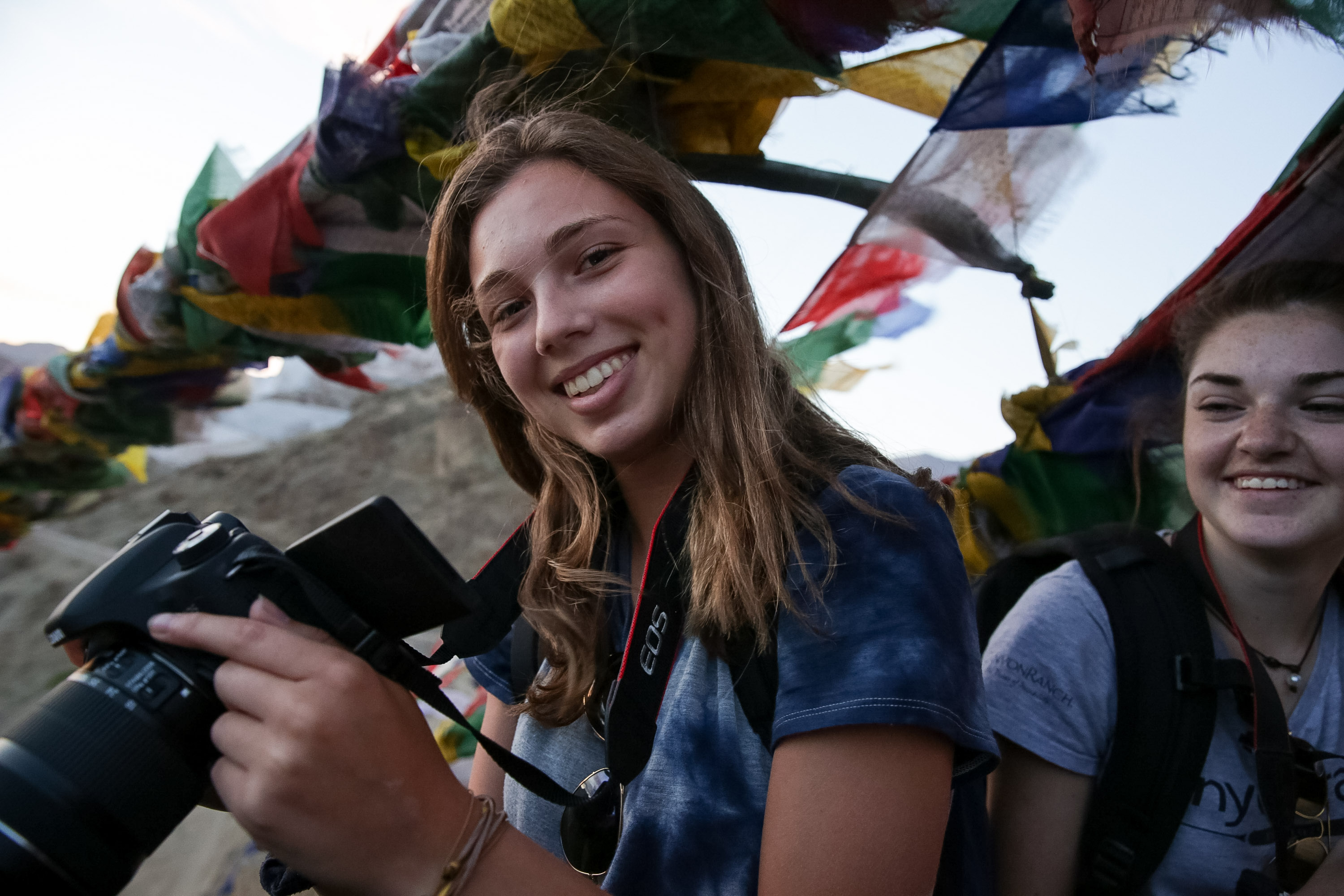 A student holds a camera beneath colorful prayer flags in Nepal