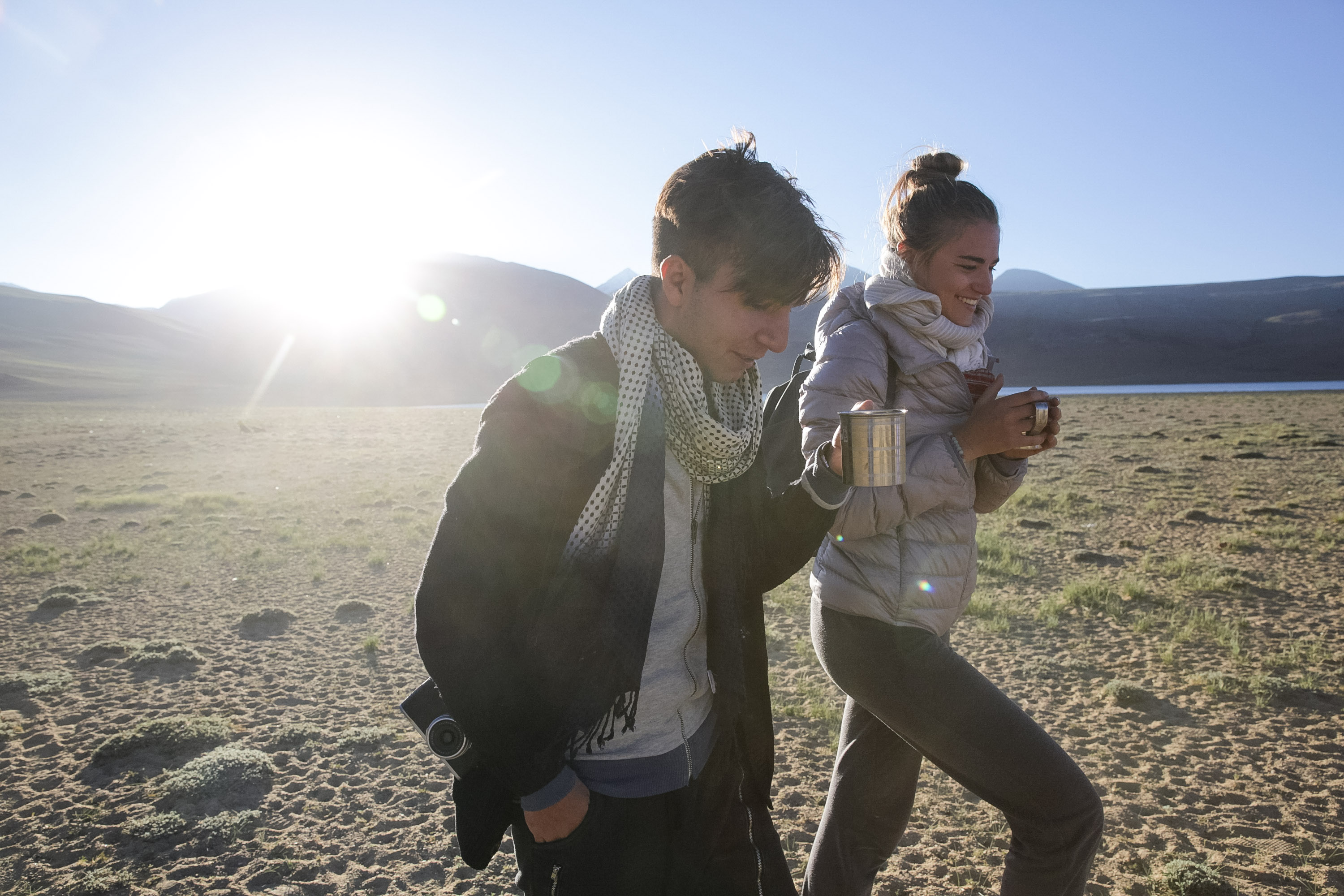 Students walk across open ground with mountains and a lake in early morning light