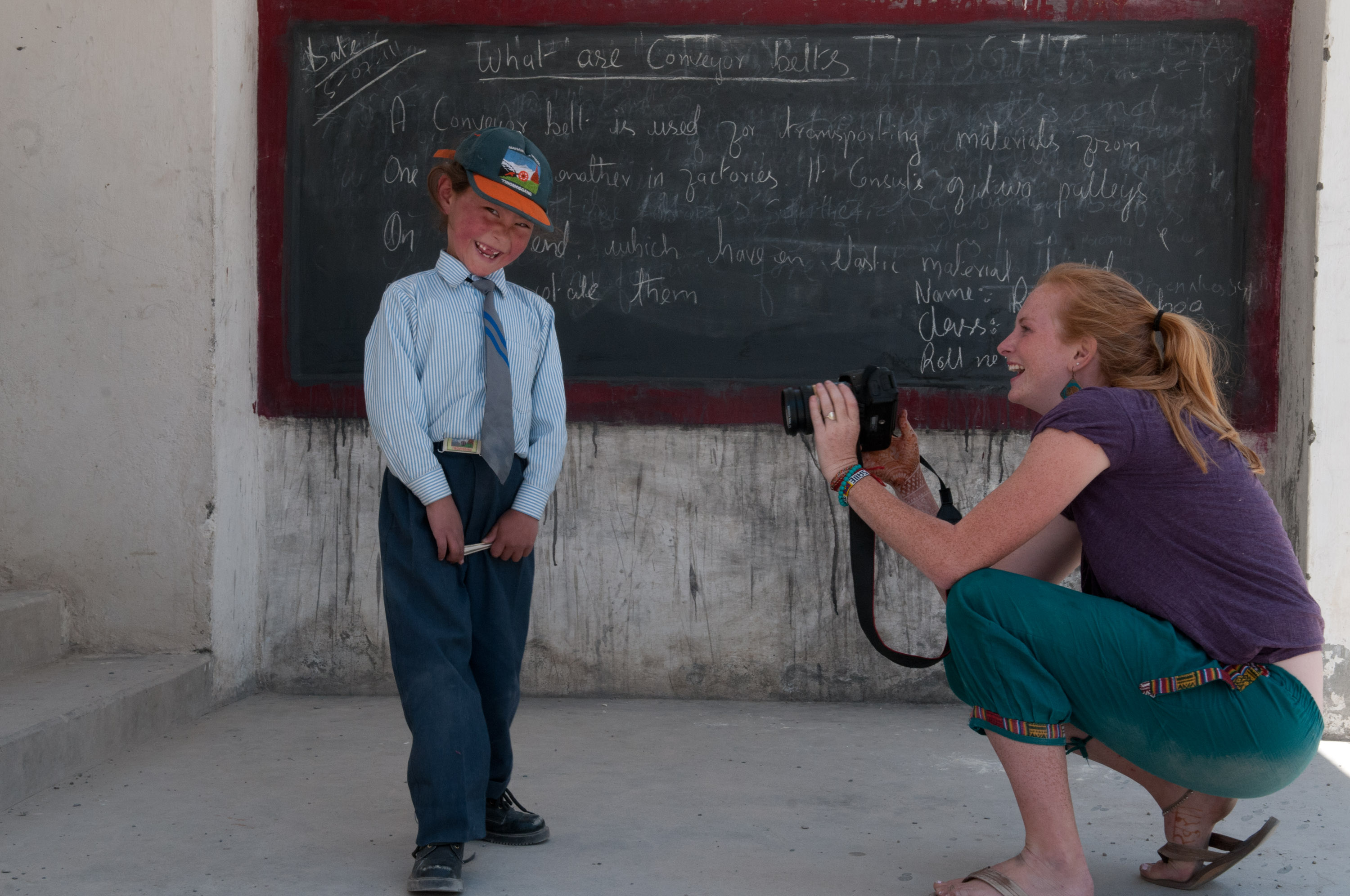 A student photographs a local boy in uniform posing in front of a chalkboard