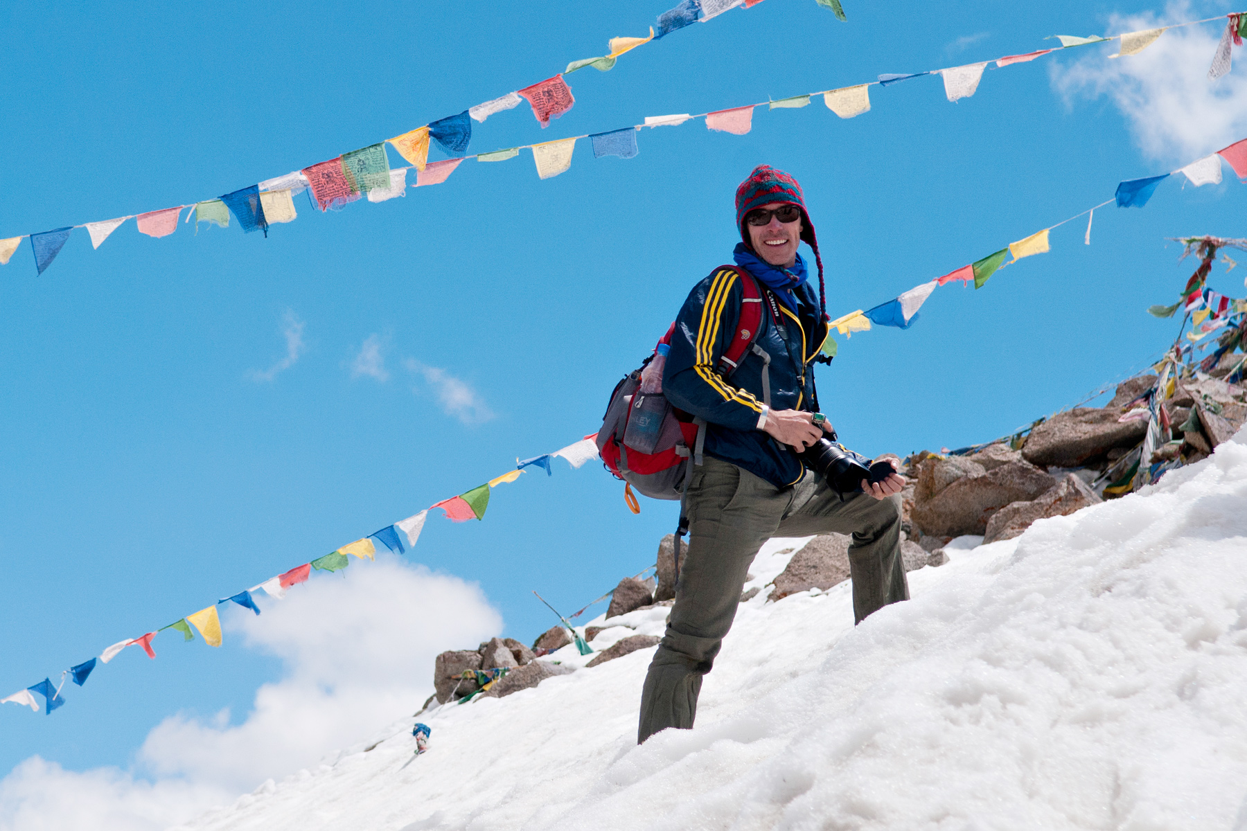 A student stands on a snowy slope beneath strings of Buddhist prayer flags