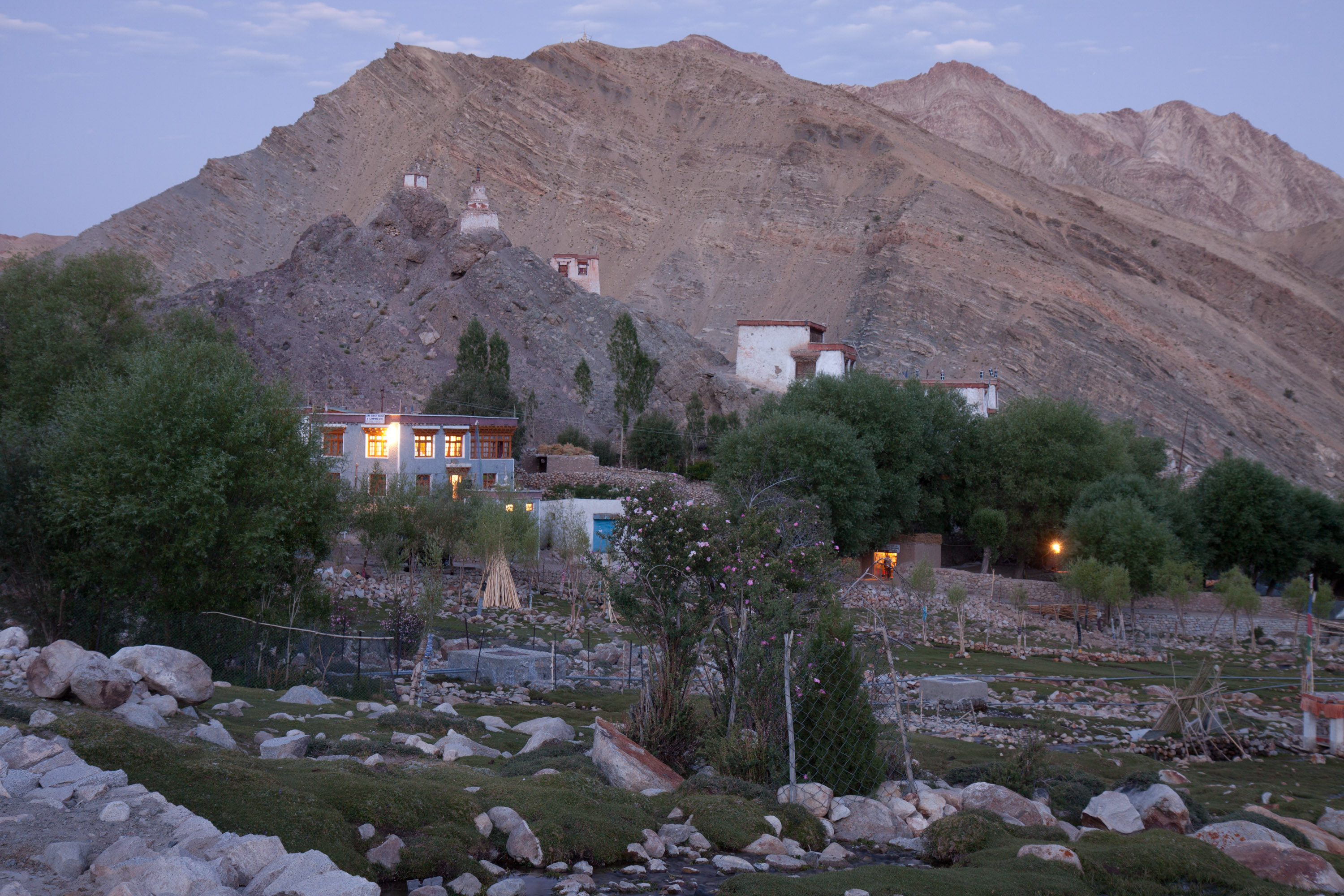 A mountain village with lit homes and terraced fields at dusk beneath rocky peaks