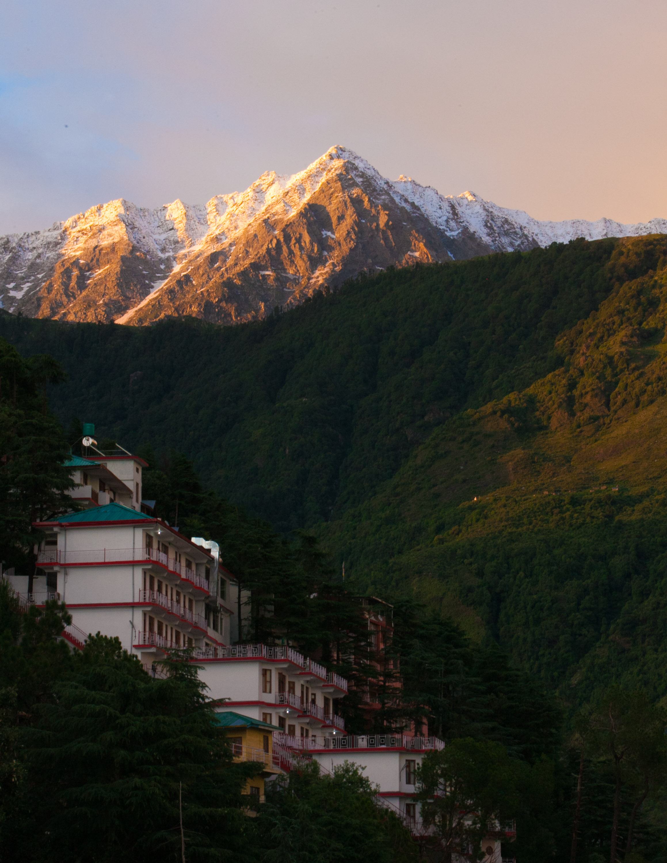 A school trip to India pauses as snow-capped Himalayan peaks rise above a hillside town at sunset