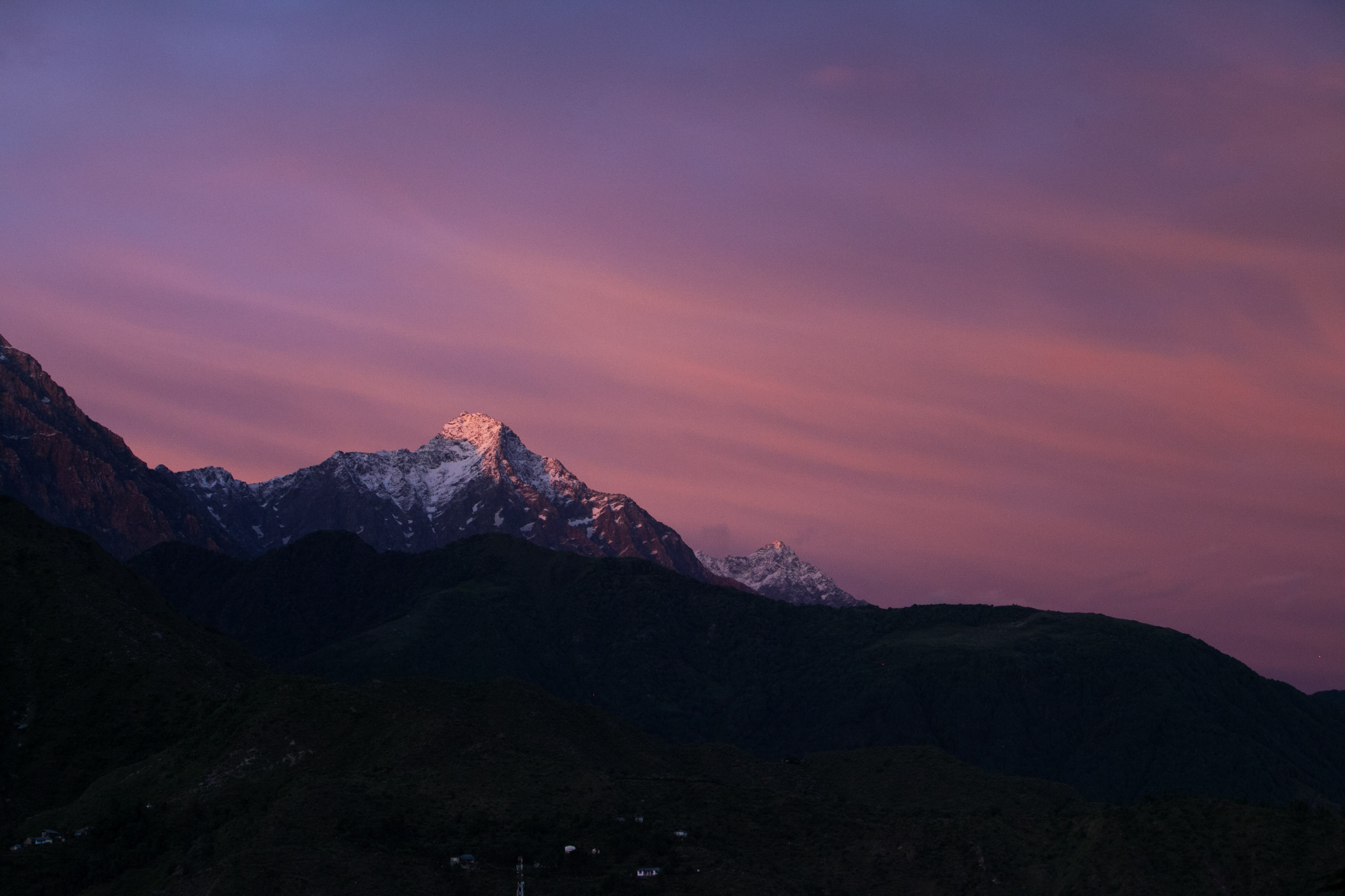 Snow-capped Himalayan peaks glow at sunset under a pink and purple sky