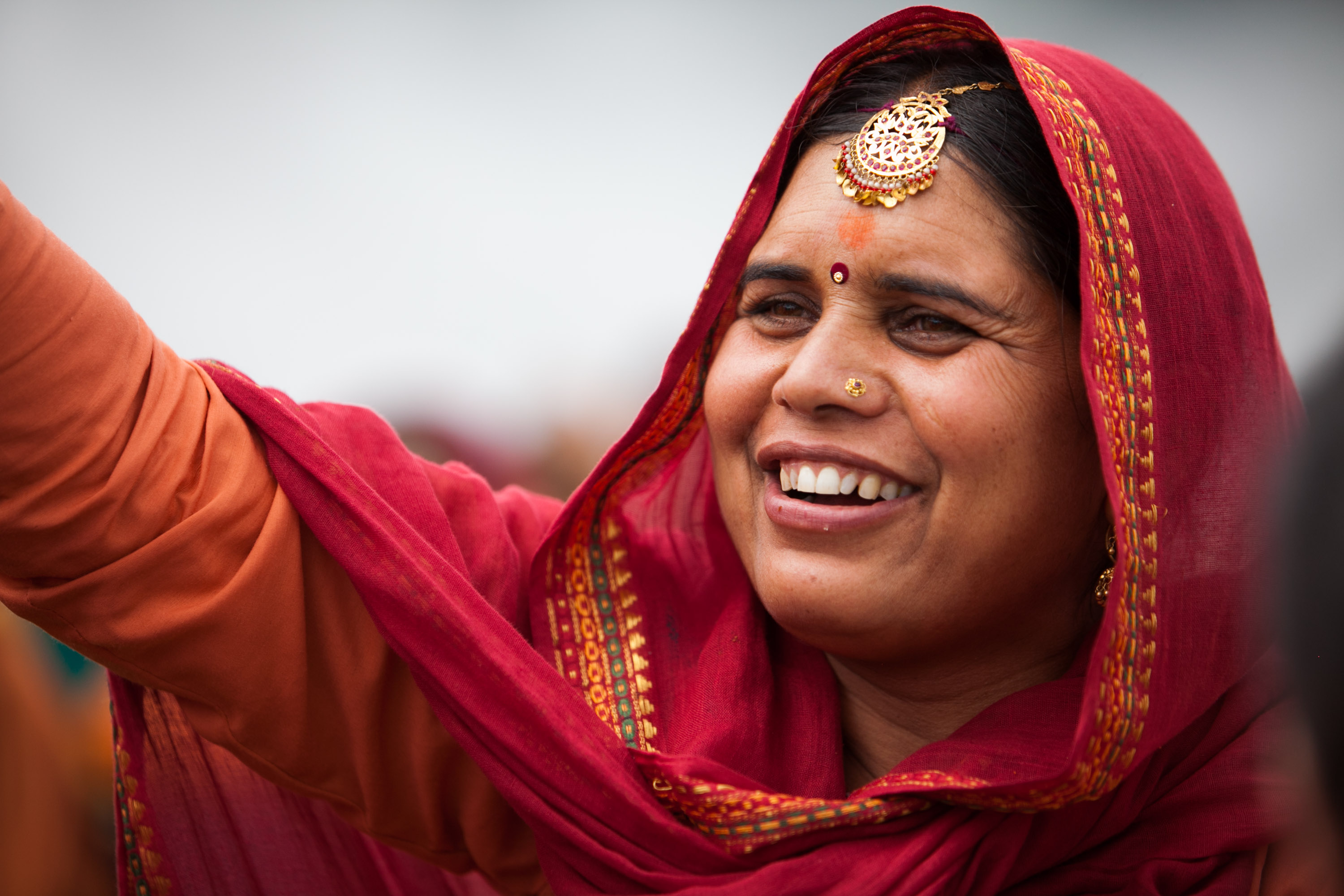 A woman in a red headscarf smiles while gesturing upward