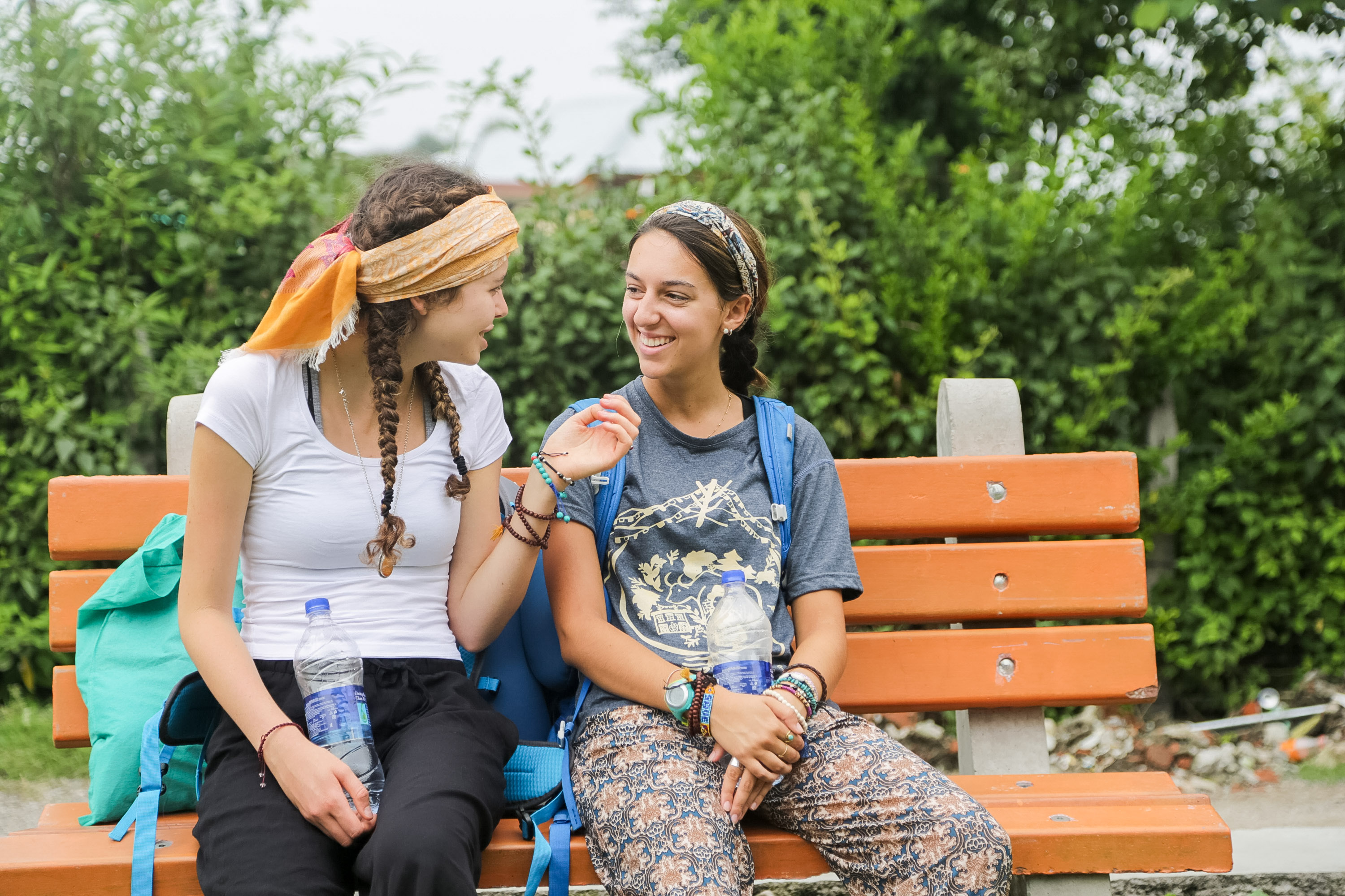 Students chat on a bench with backpacks beside them
