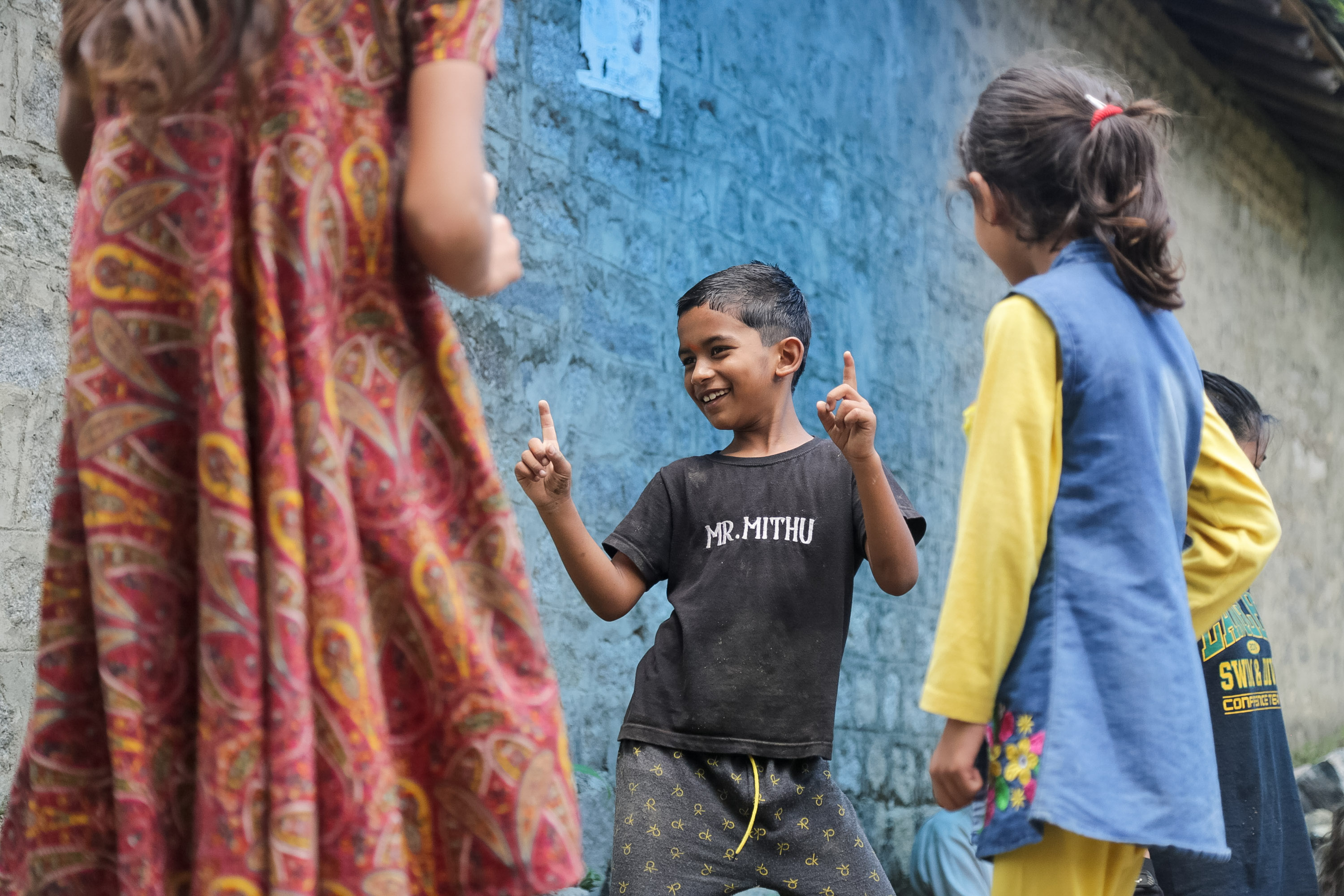 A boy laughs while making a peace sign in a village alley