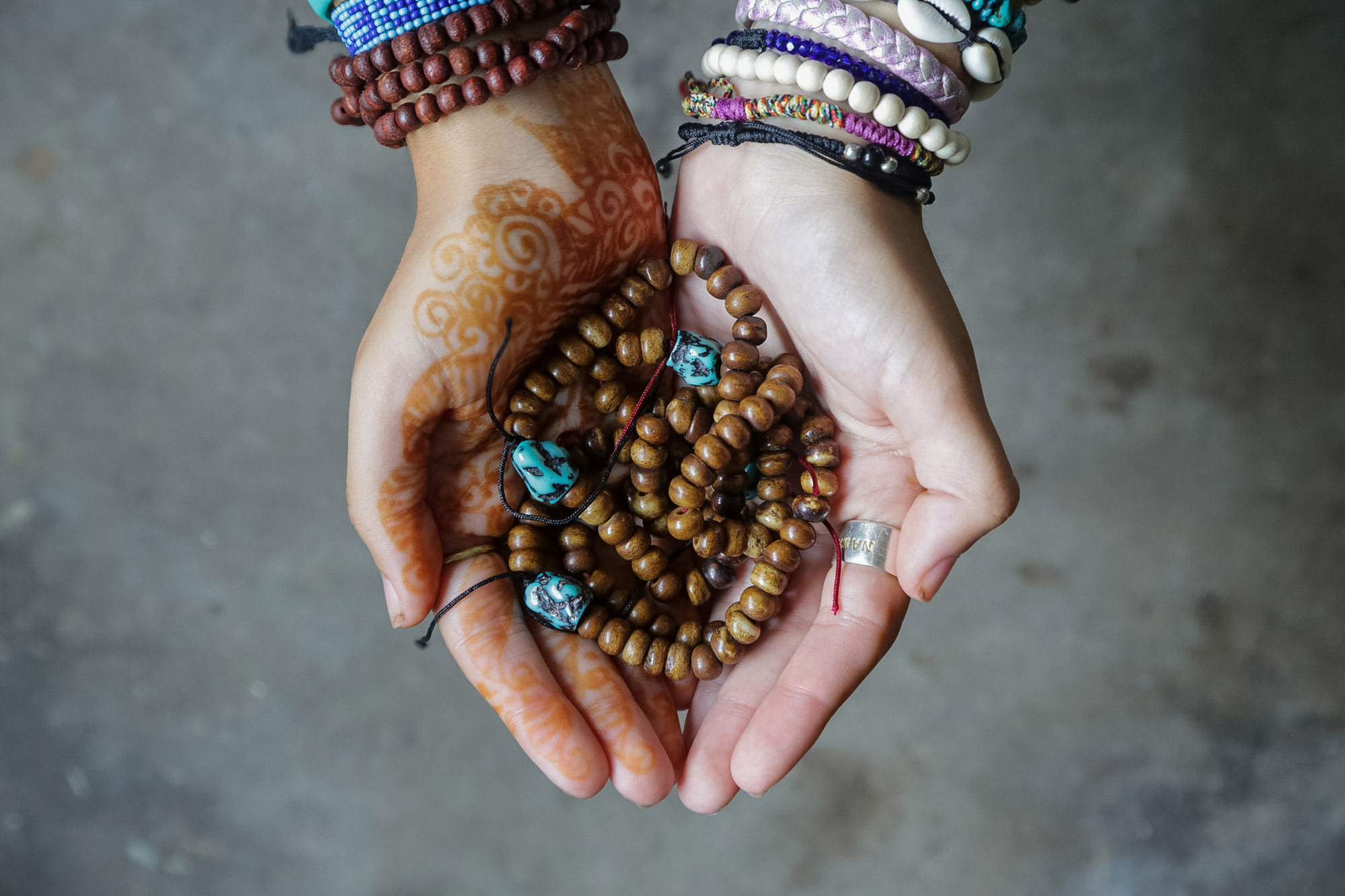 Cupped hands with henna and beaded bracelets hold a strand of wooden prayer beads