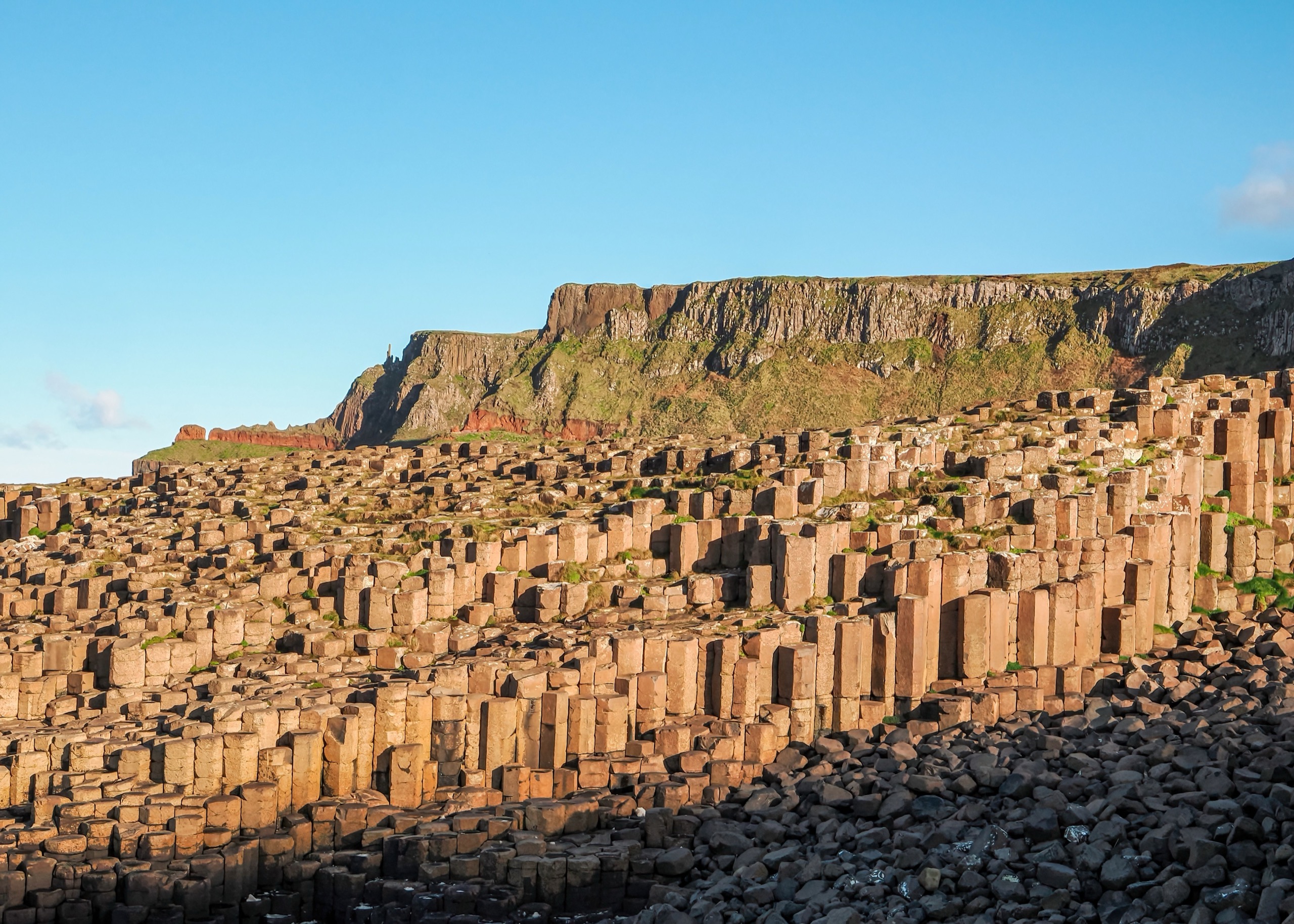 Thousands of tightly packed hexagonal basalt columns catch low golden light beneath a headland at the Giant's Causeway.