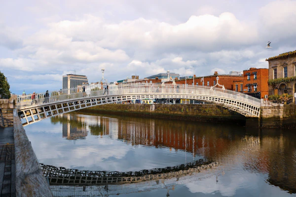 The white cast-iron arch of the Ha'penny Bridge spans the River Liffey in Dublin, its reflection in the still water