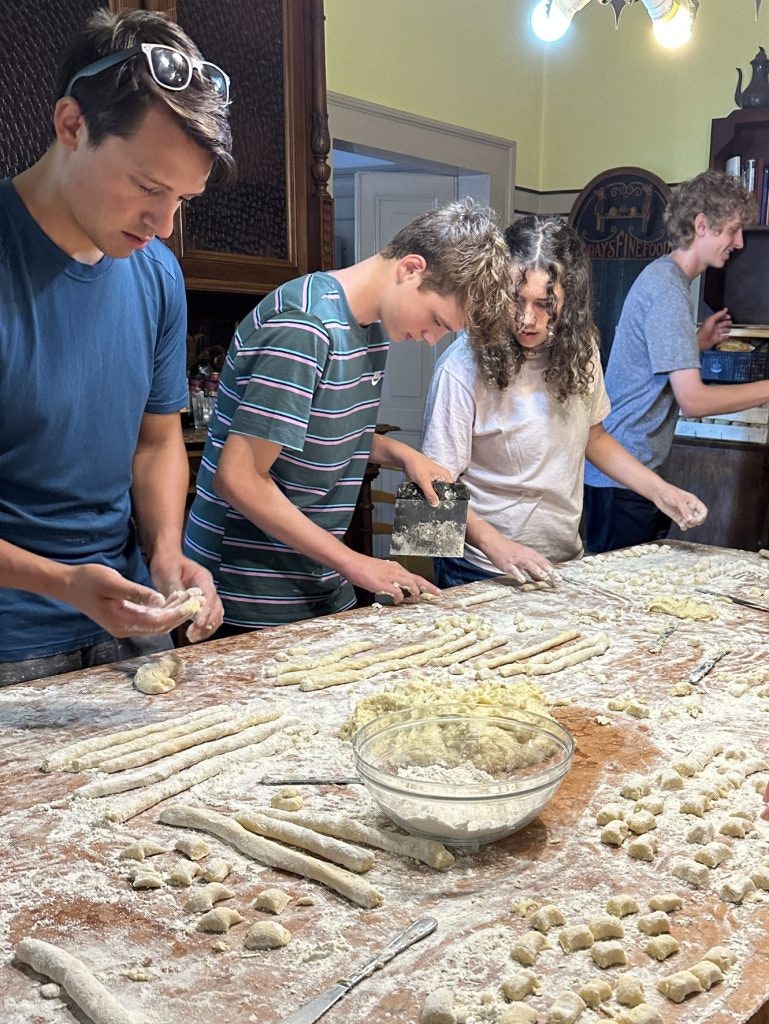 Students rolling and shaping fresh pasta dough on a flour-covered table in a rustic Italian kitchen, one of the best things to do in Italy.