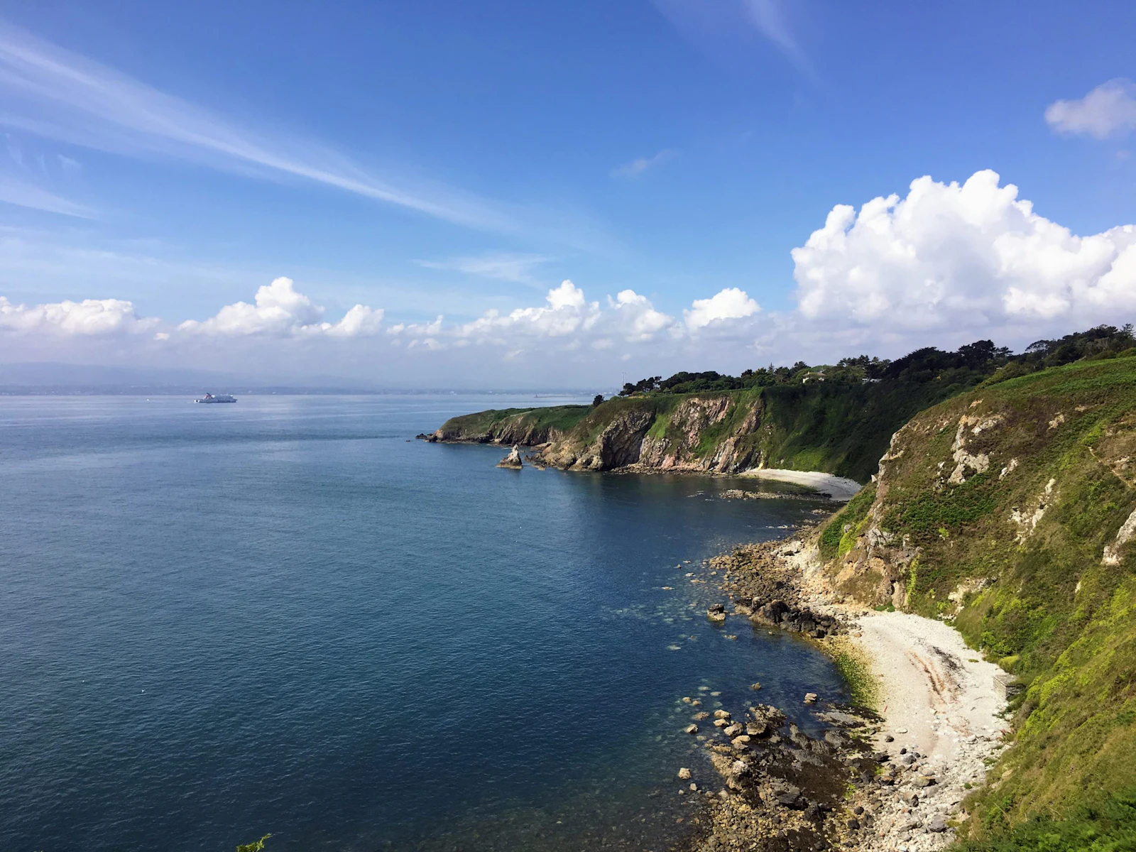 Green headlands and a pale shingle cove line a deep blue bay on the Irish coast