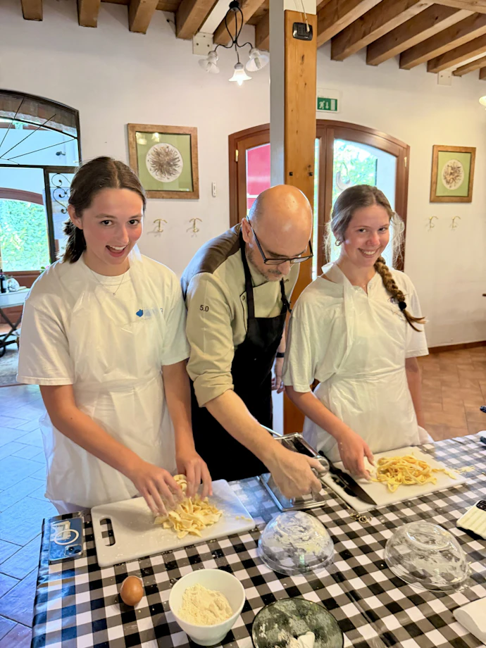 Two teen travelers shape fresh pasta beside a chef during a cooking class in Italy