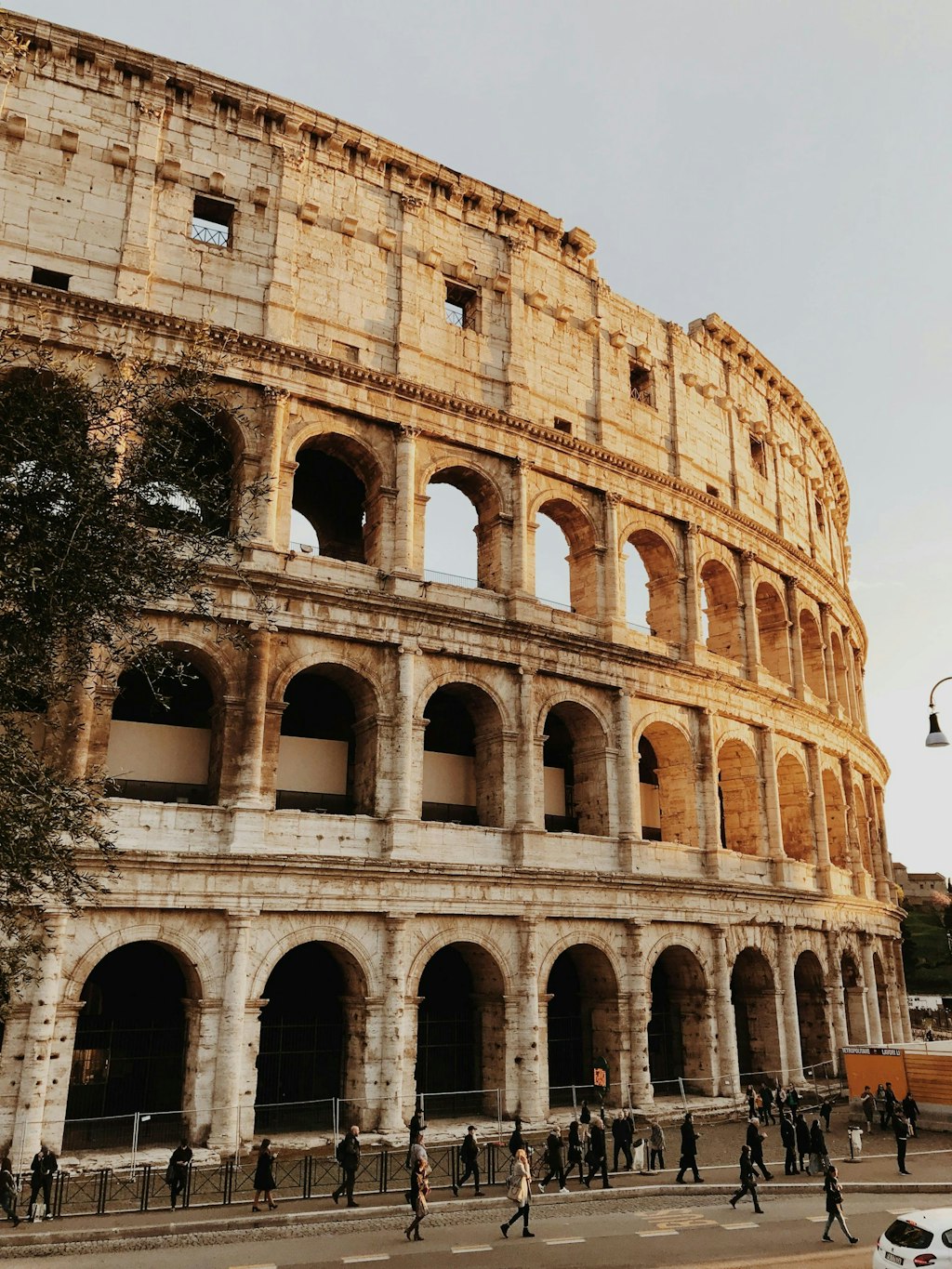 The Colosseum in Rome with its iconic arches illuminated by the golden glow of the setting sun, as people walk below.