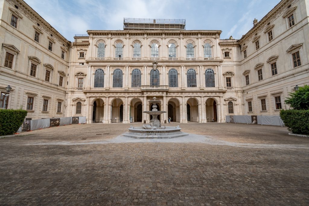 The grand courtyard of a historic Italian palace with a central fountain.