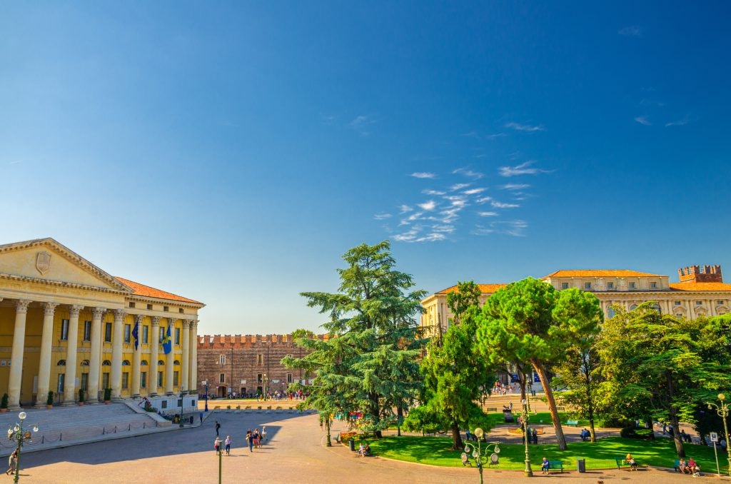 A sunny plaza in Verona with neoclassical and medieval architecture.