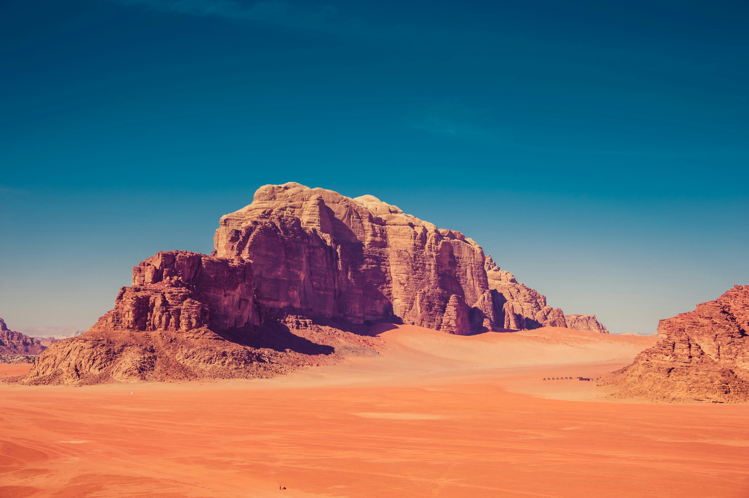Flat orange sand runs to a broad sandstone massif under a deep blue sky.