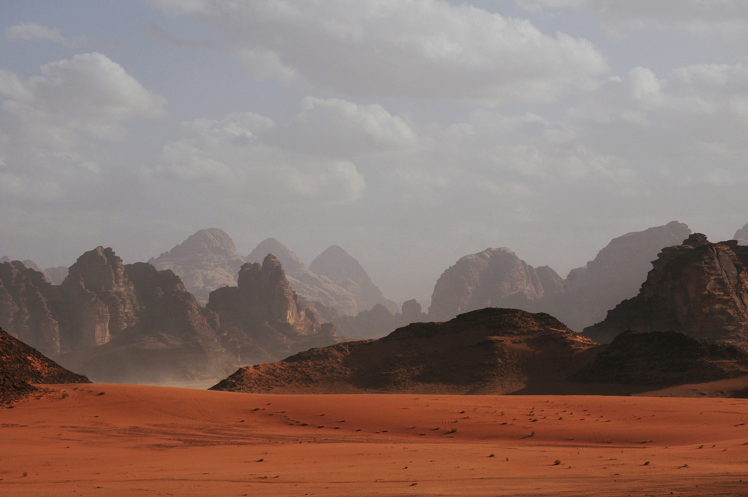 Red sand drifts toward a line of jagged mountains under a hazy sky.