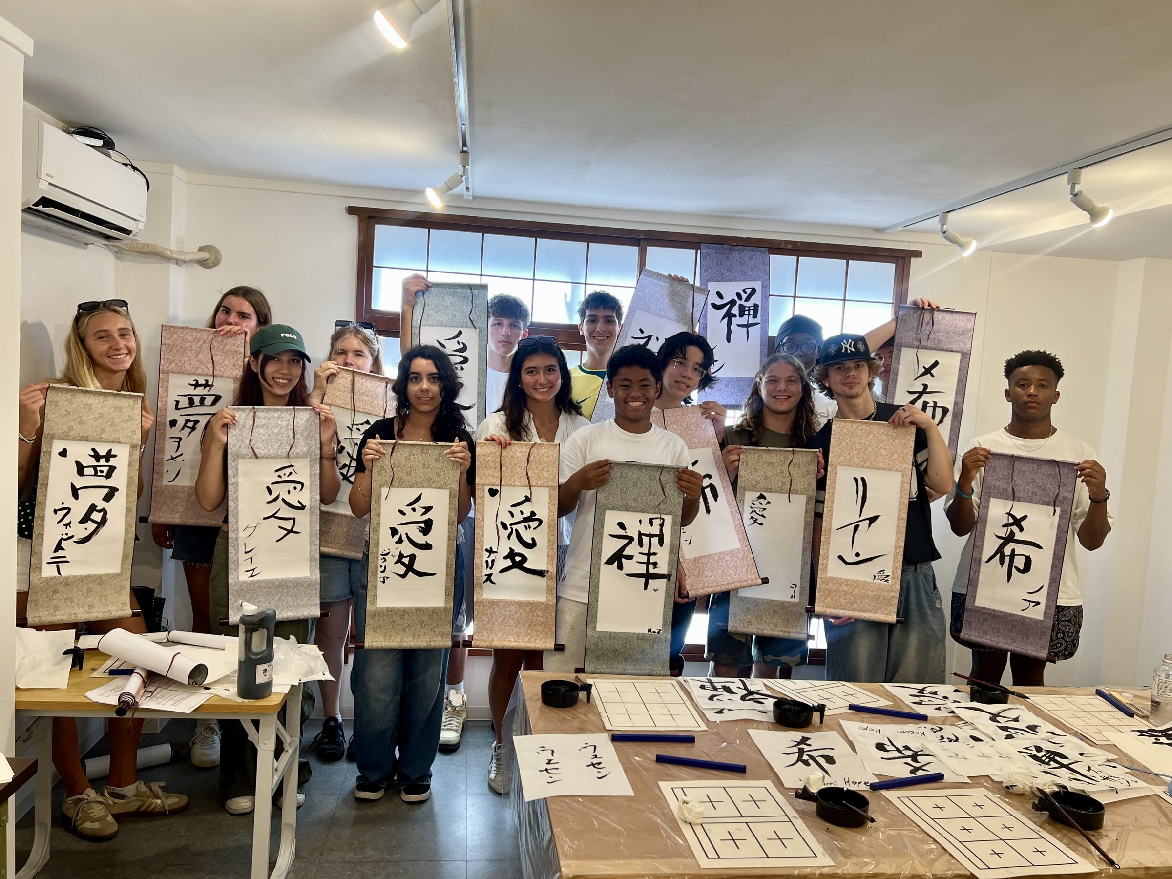 Students hold up finished calligraphy scrolls, the brushed kanji still drying
