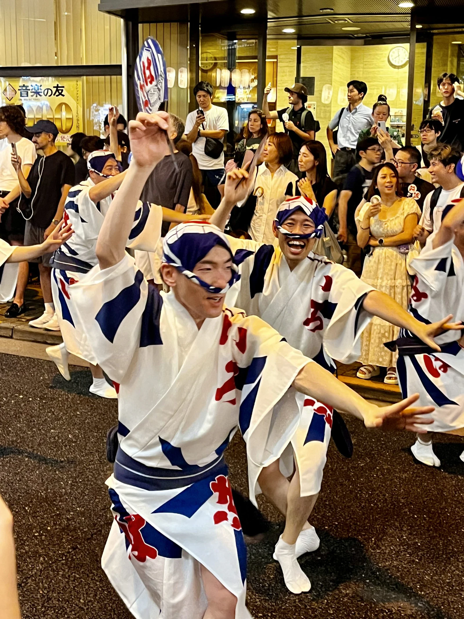 Dancers in happi coats and headbands move through a night street festival, arms raised.