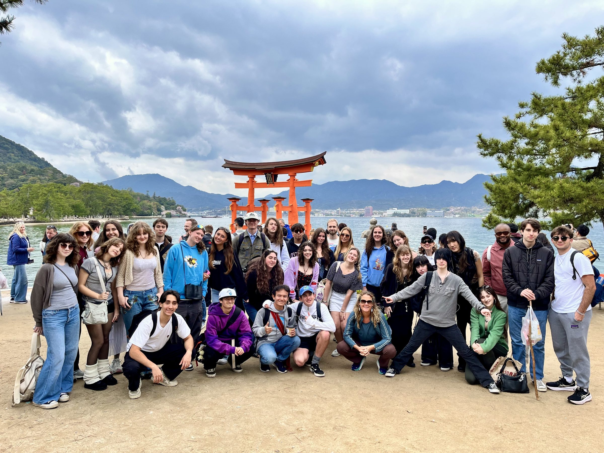 A school group gathers on the shore at Miyajima in front of the floating torii of Itsukushima Shrine
