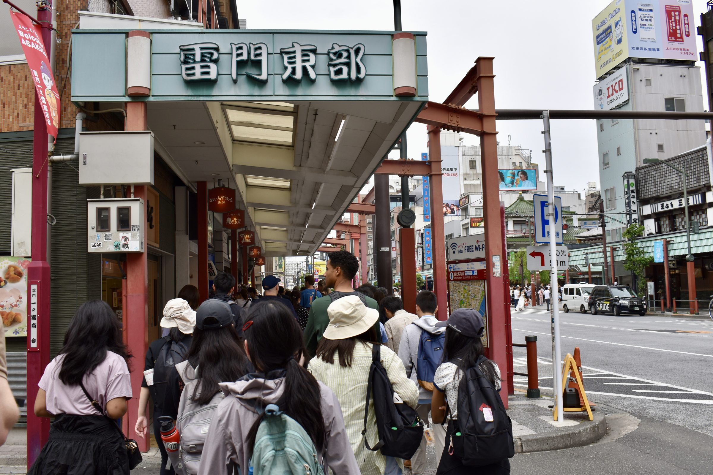 Students walk as a group past shop signs and a red torii gate in the Asakusa district
