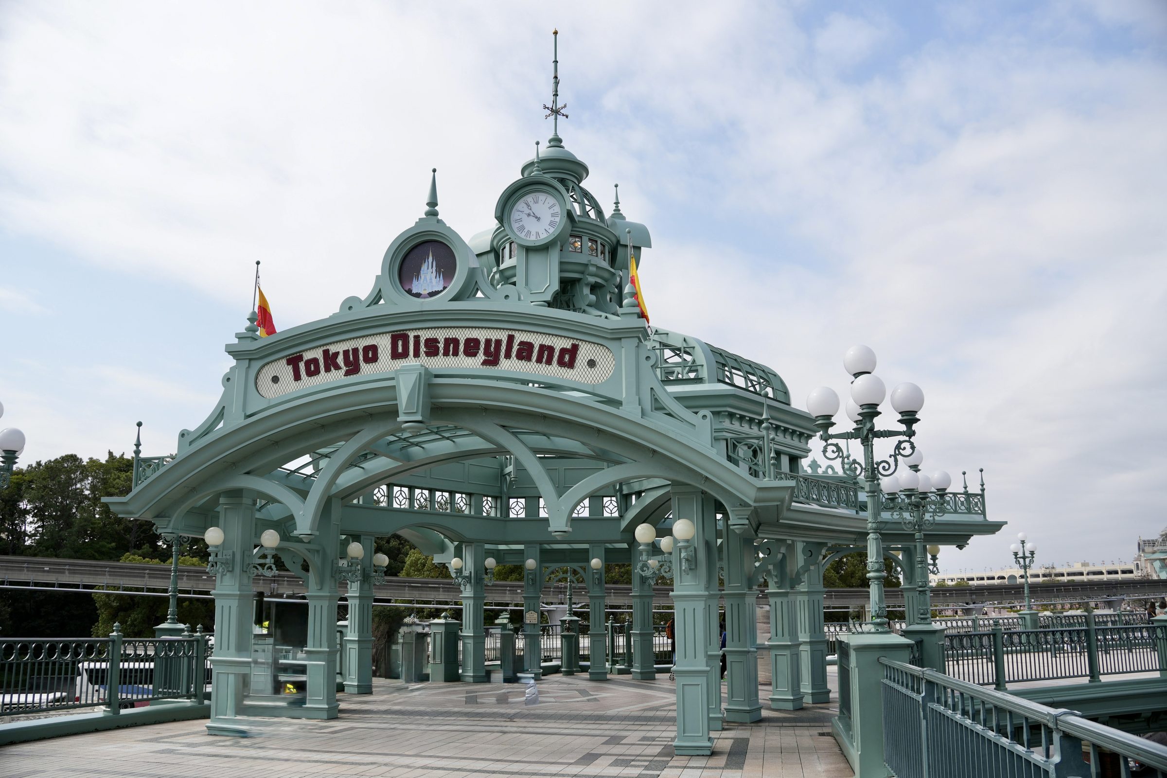 The pale green ironwork entrance pavilion at Tokyo Disneyland, its clock tower under a bright sky