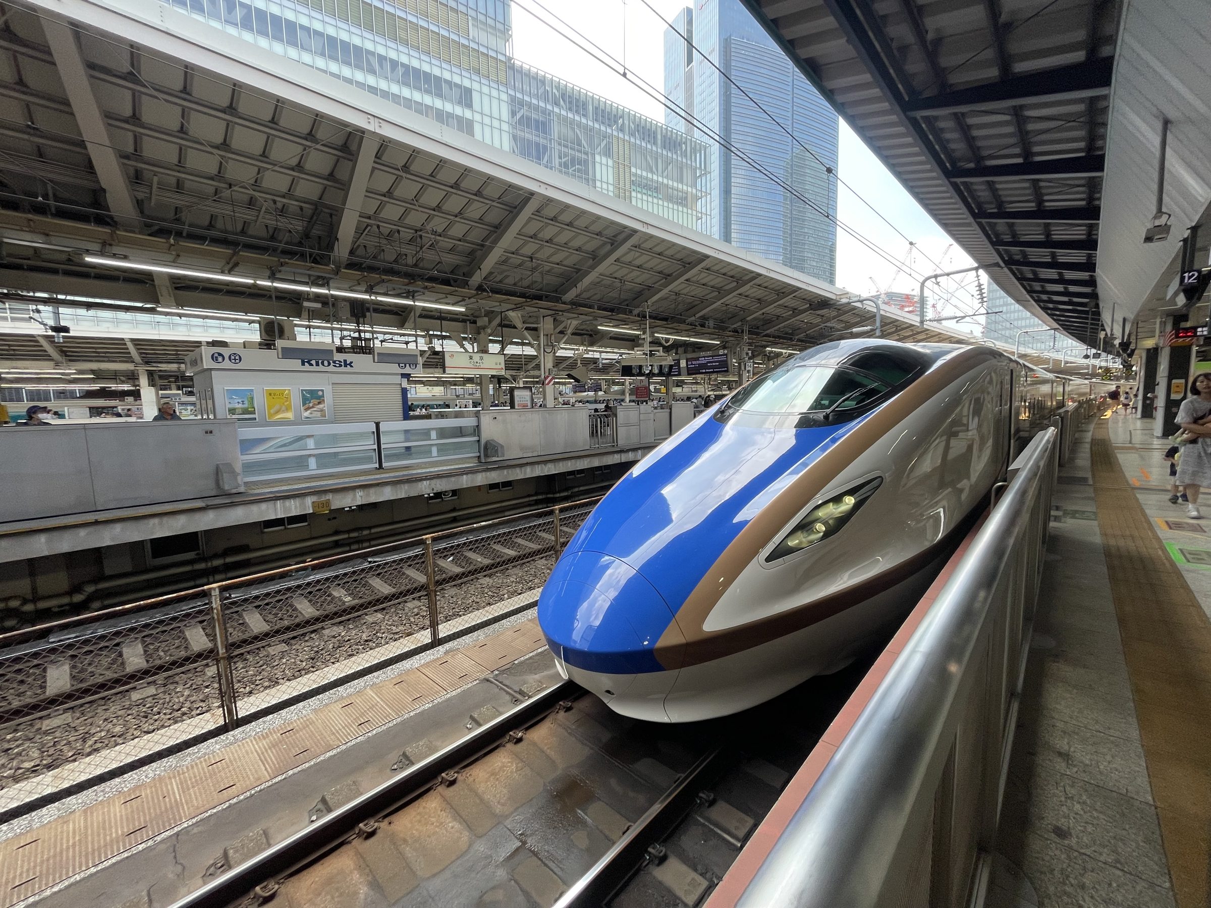 A Shinkansen waits at a Tokyo Station platform, its blue and white nose angled along the track