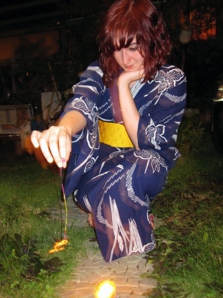 A girl in a blue yukata plays with a traditional Japanese sparkler.