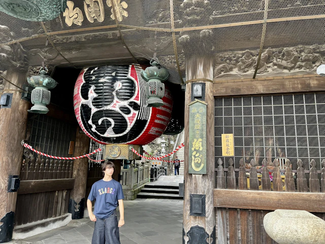 A student stands under a huge red and black paper lantern in a carved wooden temple gate in Japan