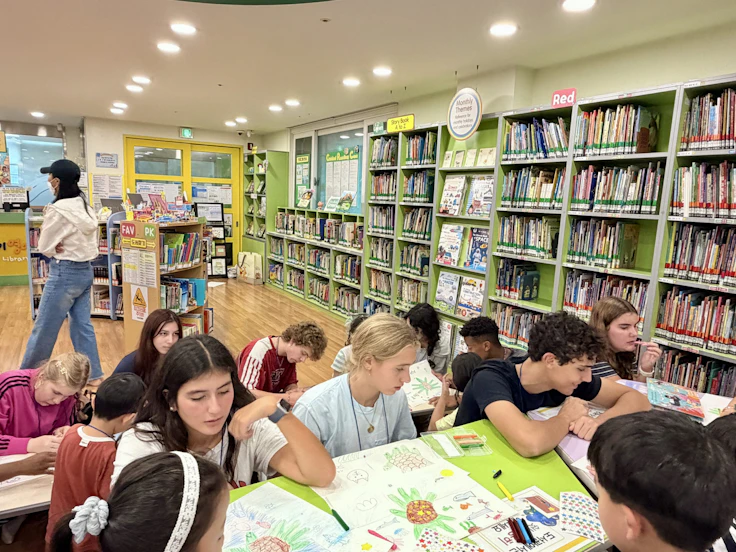 Students sit together with papers and books at tables in a library