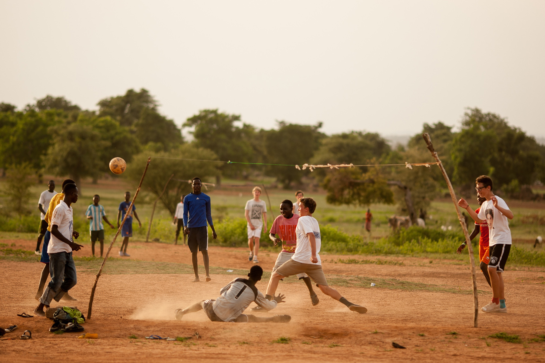 Students play a pickup soccer match with local kids on a dusty field