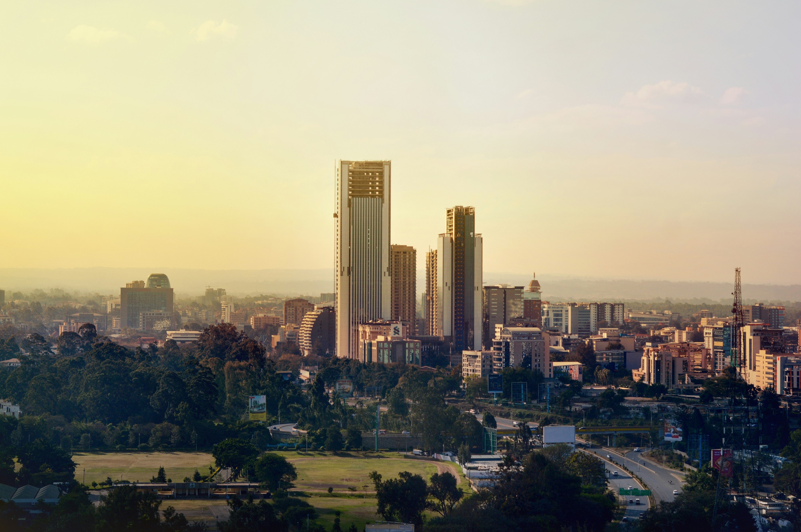 Nairobi's high-rise skyline catches the late sun above parkland and a busy road in the foreground.