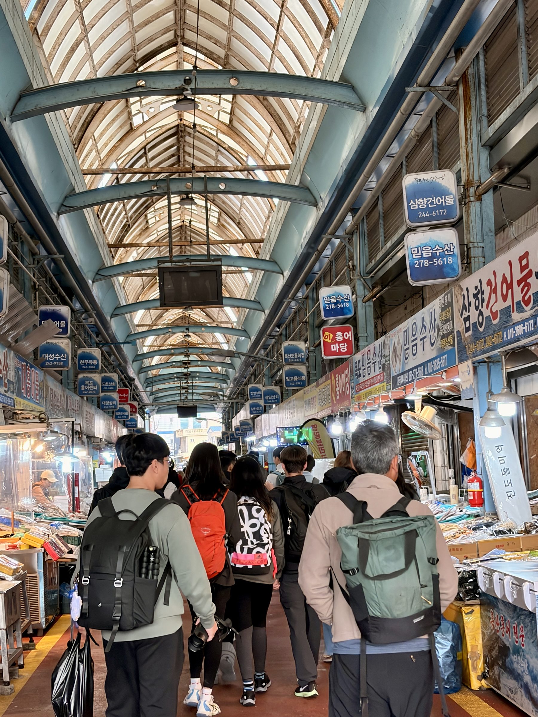 Shoppers move through a covered traditional market arcade hung with signs and awnings
