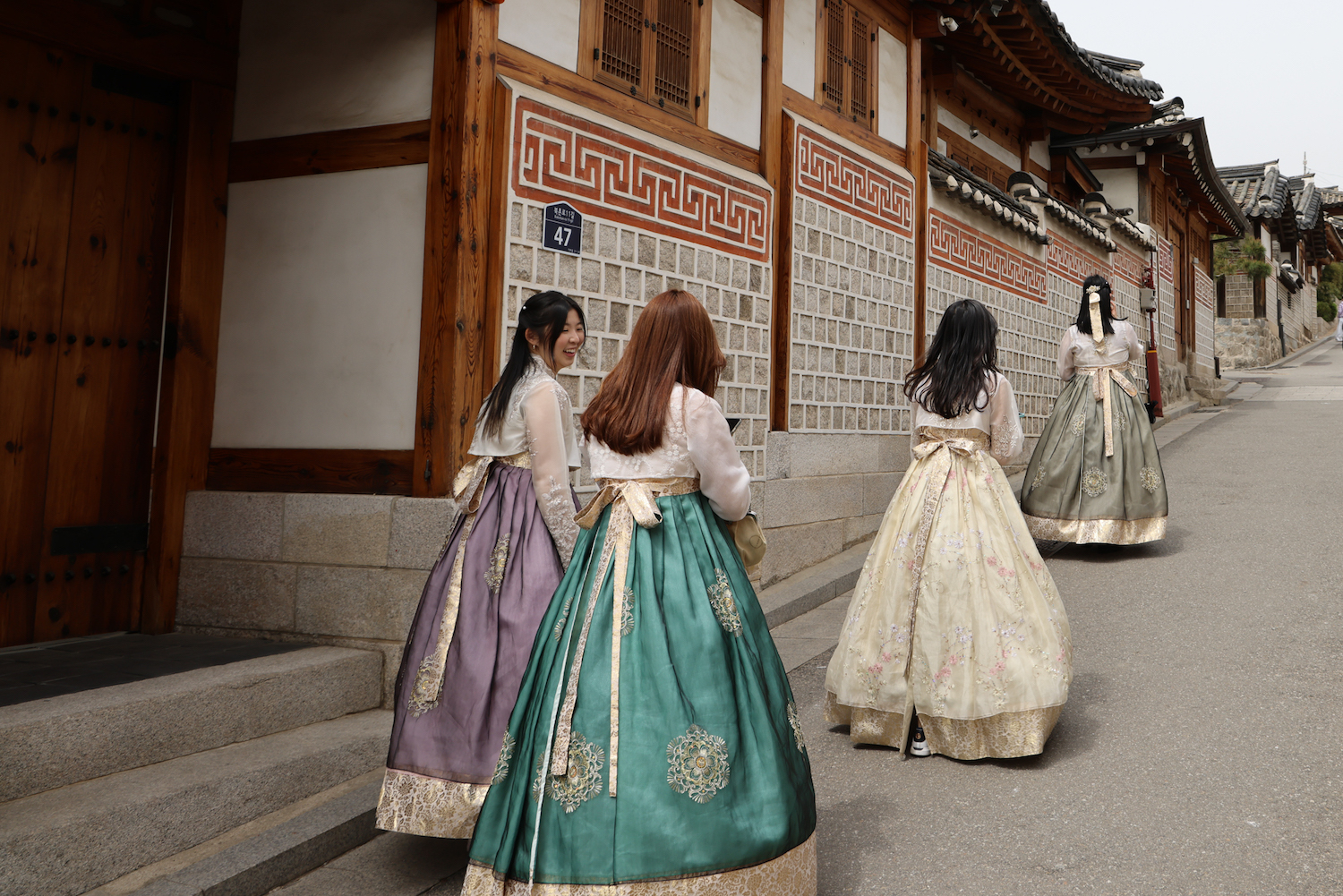 Student travelers wearing traditional Korean hanbok walking past a historic building in South Korea.