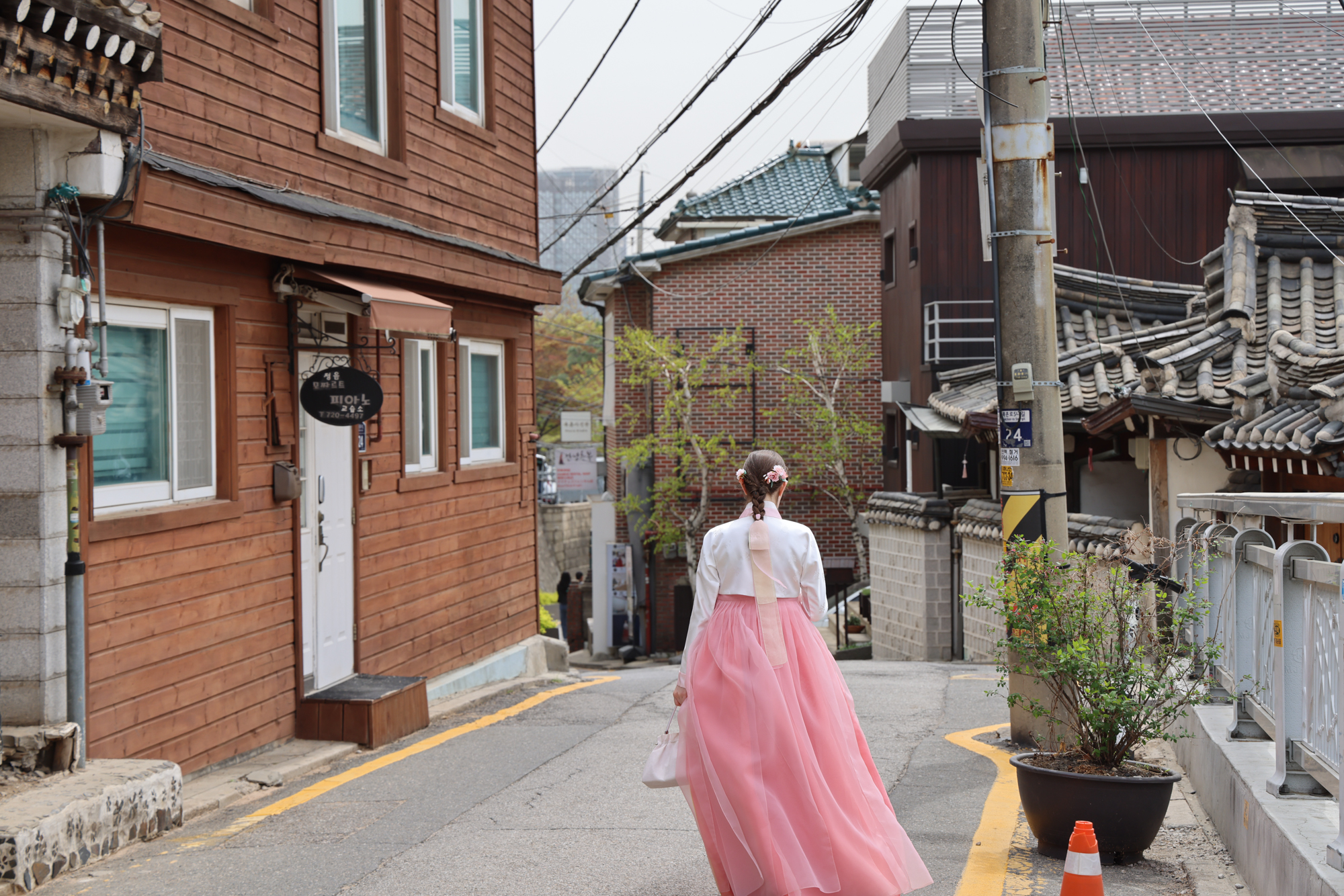 A student in hanbok walks a quiet lane of hanok houses in the Bukchon quarter