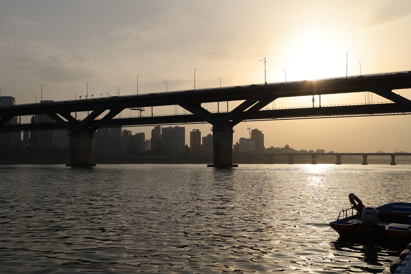 The sun sets behind a bridge over a river in Seoul