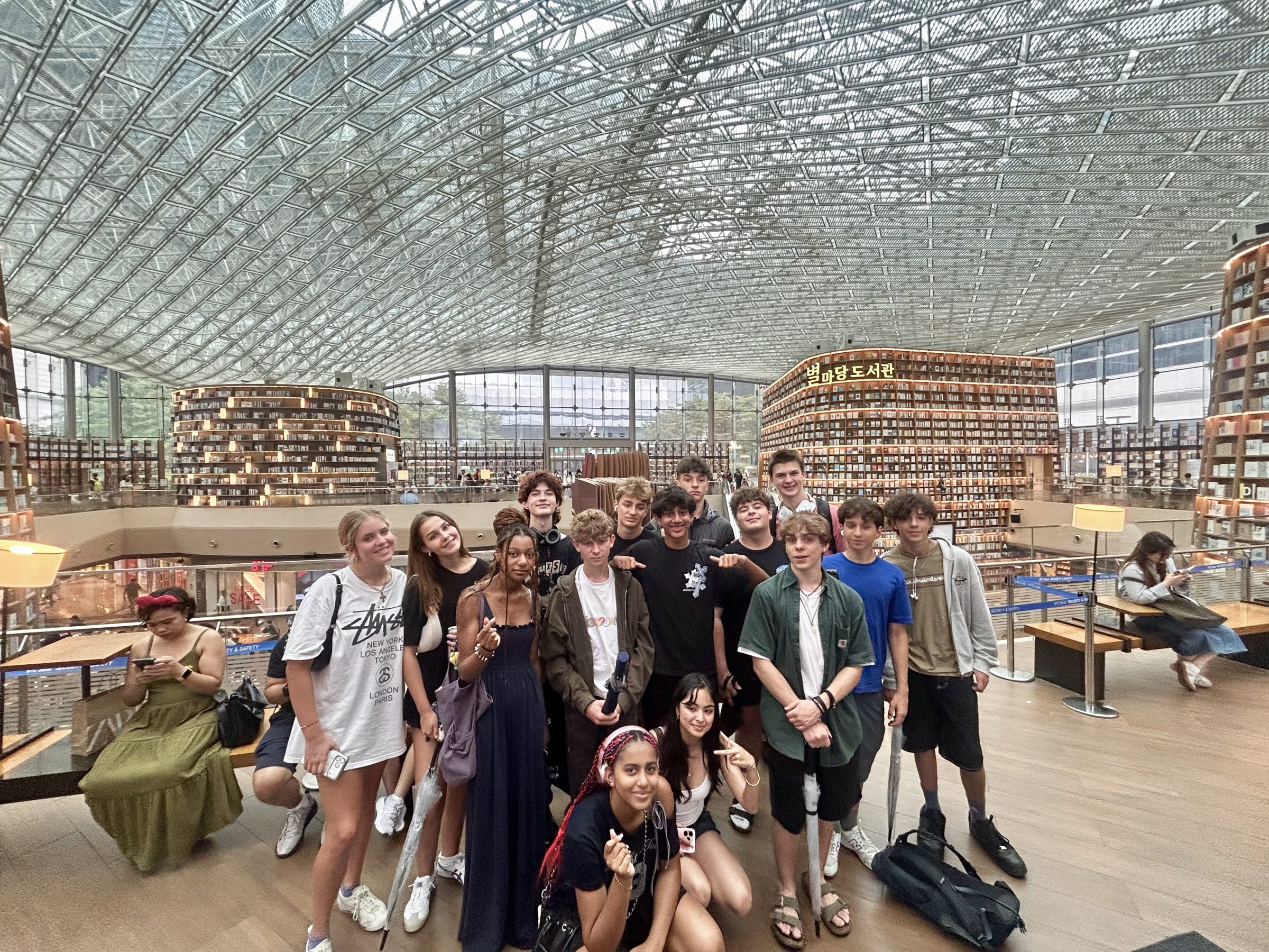 A group under the glass roof of Starfield Library, its wall-height shelves behind them