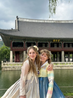 Two girls in hanbok smile and pose in front of one of the buildings at Gyeongbokgung Palace, Seoul.