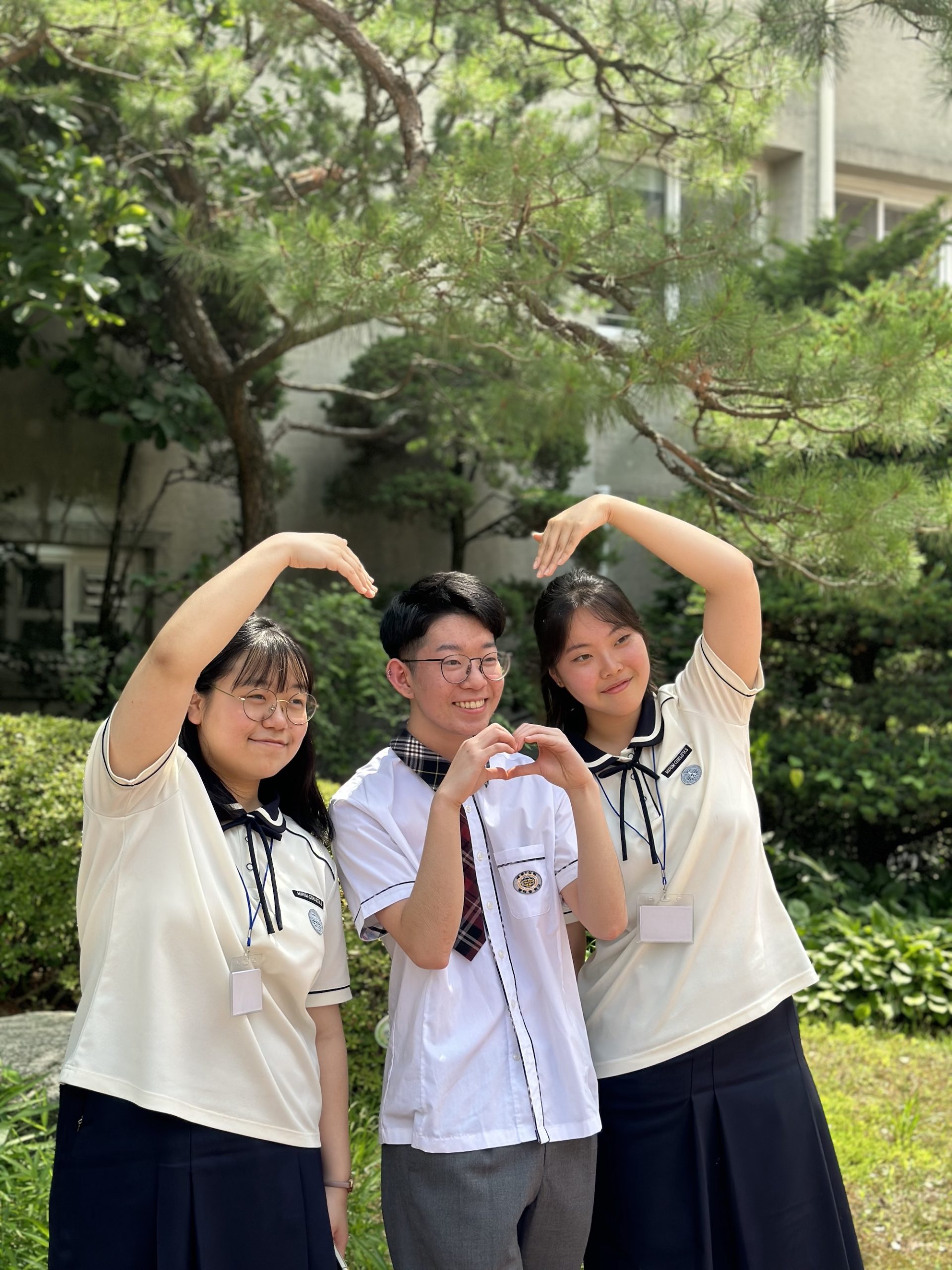 Students in school uniforms form a heart shape with arched arms in a garden
