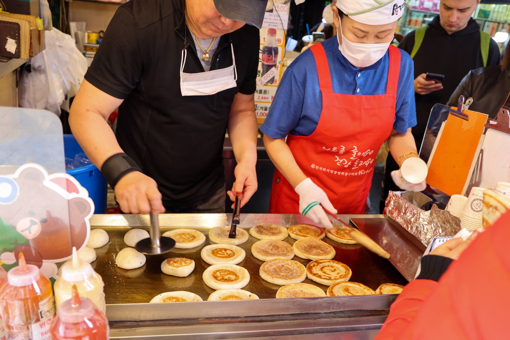 Two vendors cook hotteok on a griddle at a Seoul market stall