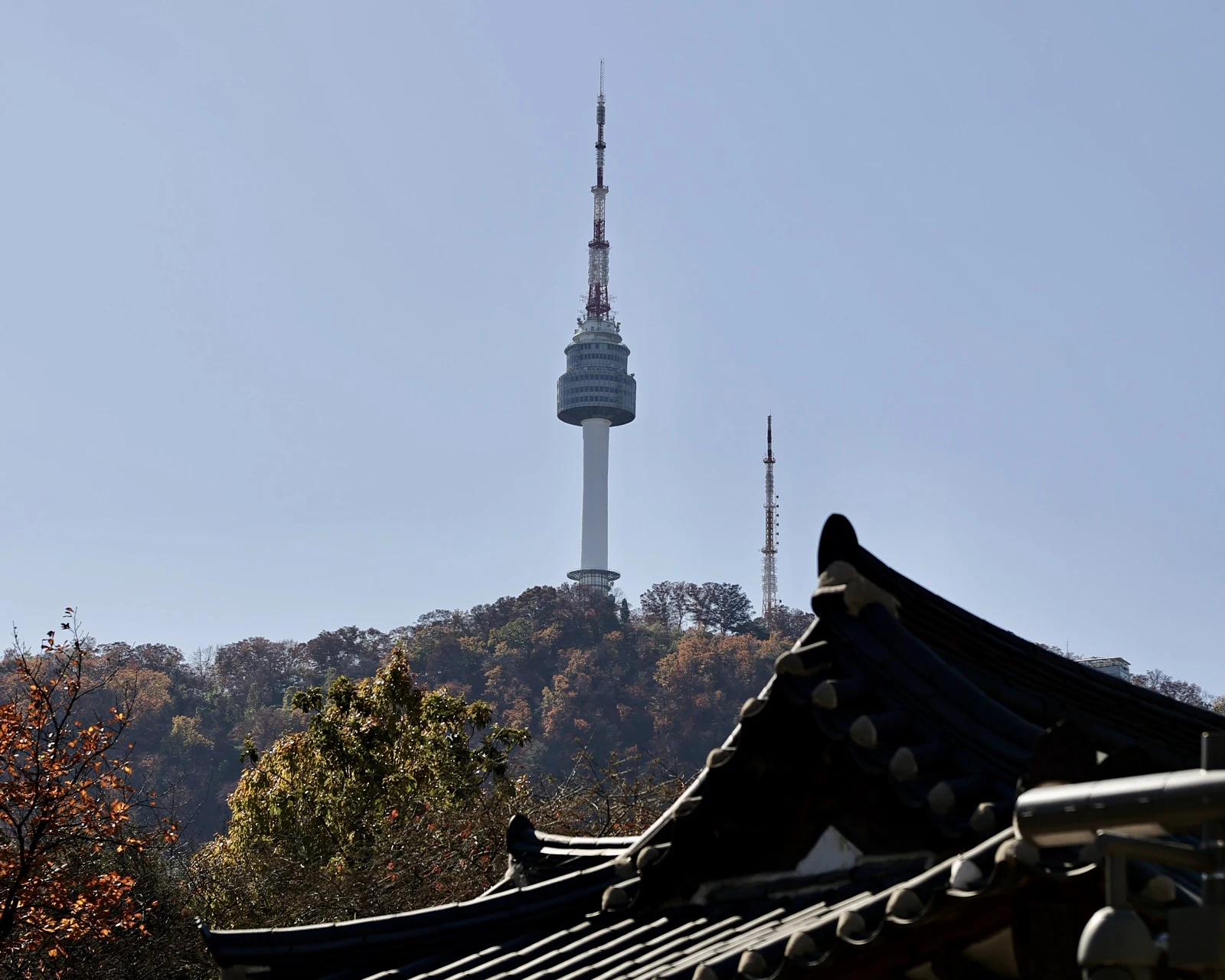 N Seoul Tower rises on Namsan behind a traditional tiled roof in Seoul