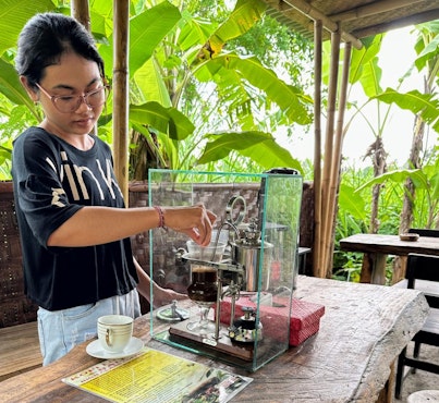 A woman preparing a cup of Kopi Luwak at a coffee farm in Bali, using traditional brewing methods.